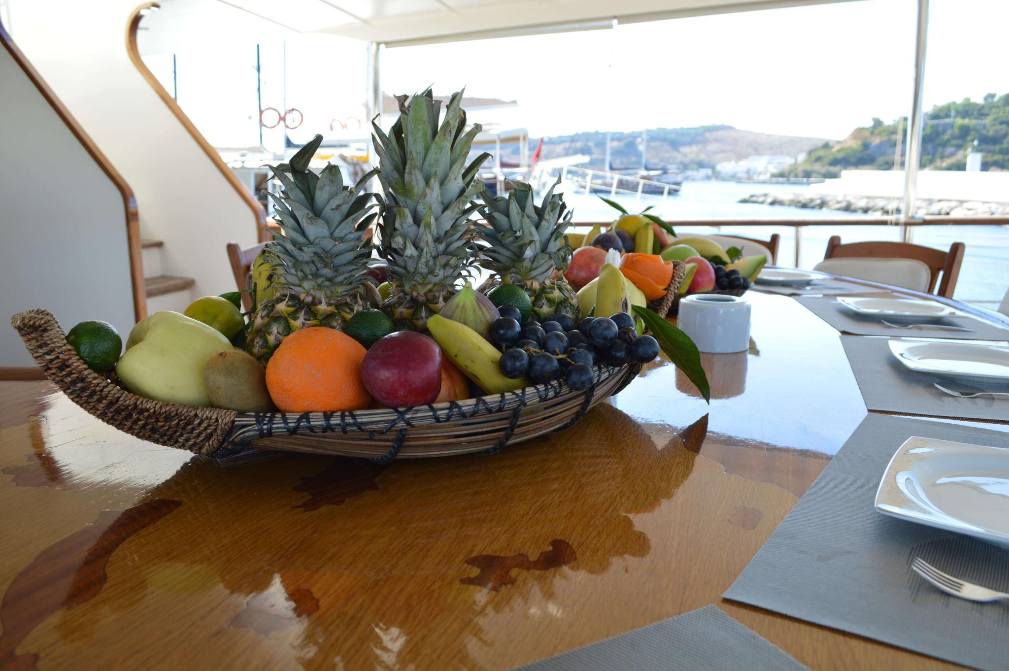 large wicker fruit basket with pineapples and tropical fruits on yacht dining table with harbor view