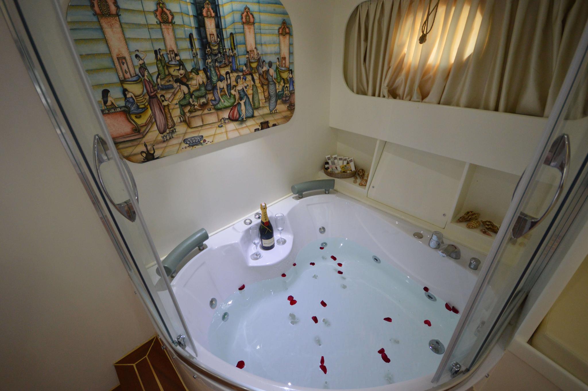 yacht jacuzzi filled with water, champagne bottle and scattered red rose petals