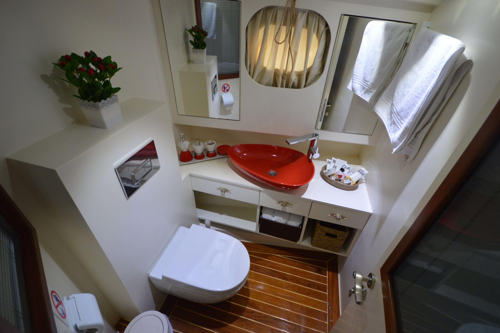 yacht bathroom featuring red ceramic vessel sink, white vanity with storage, and teak flooring