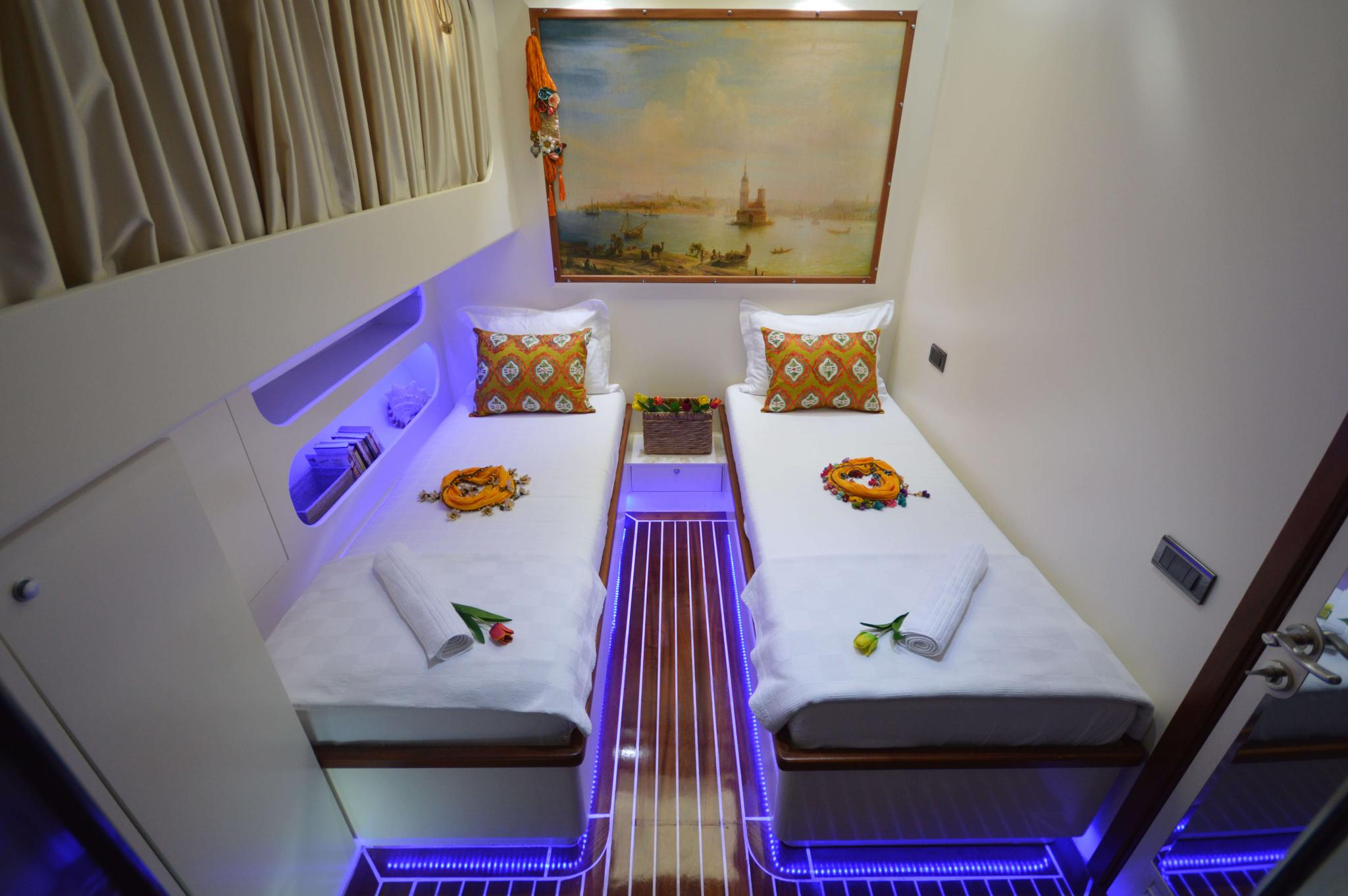 guest cabin featuring twin beds with white linens, purple LED strip lighting, and maritime artwork