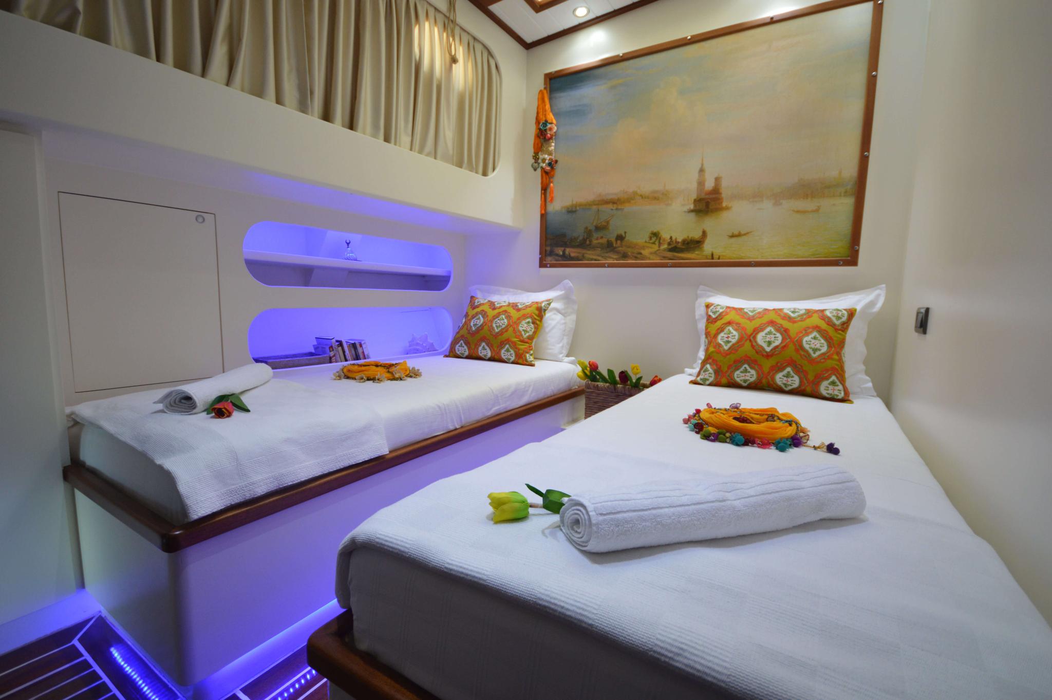 yacht guest cabin featuring two single beds with white linens, colorful decorative pillows, purple LED lighting, and framed artwork