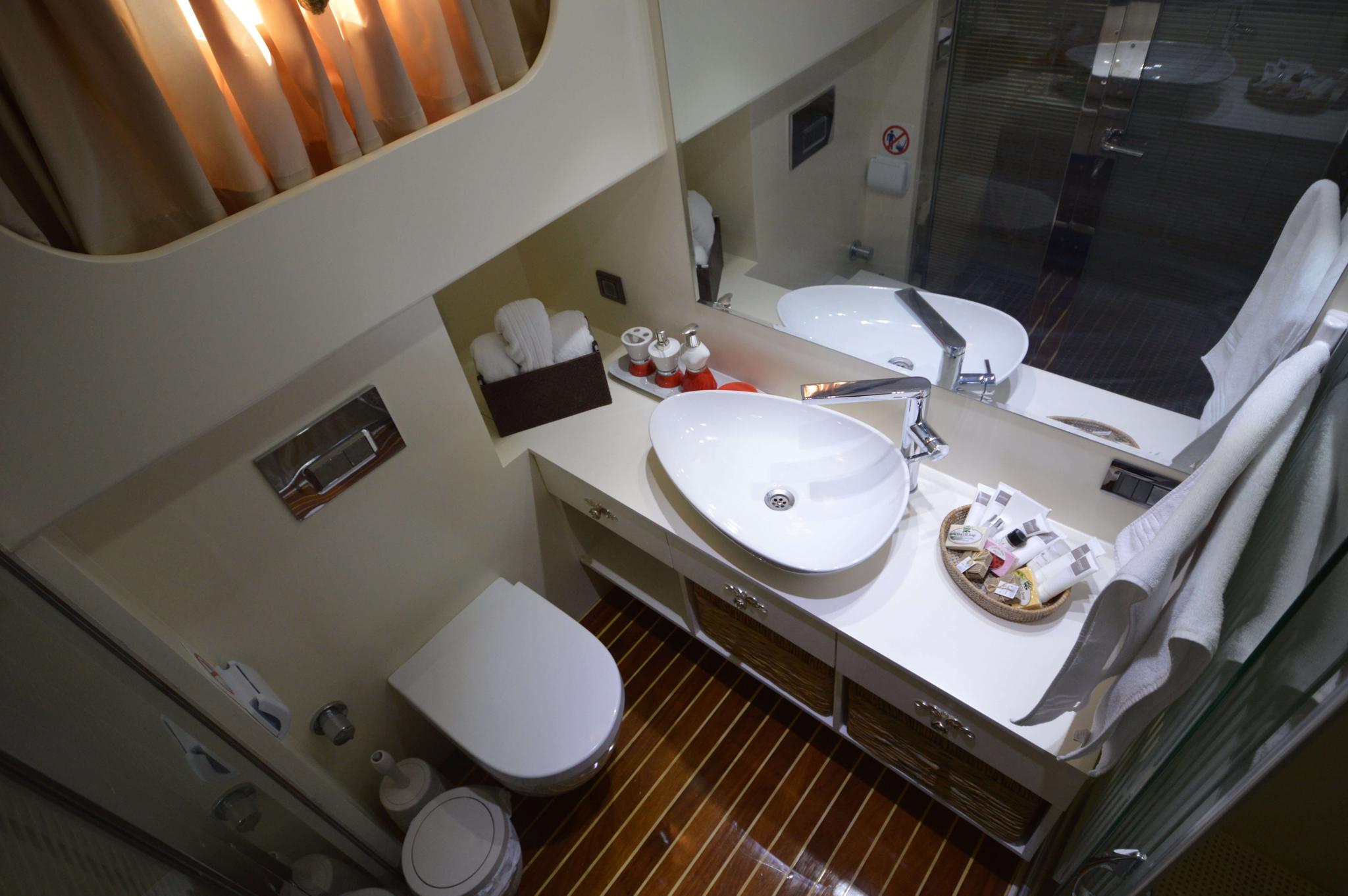 yacht ensuite bathroom with oval sink, toilet, glass shower and teak flooring