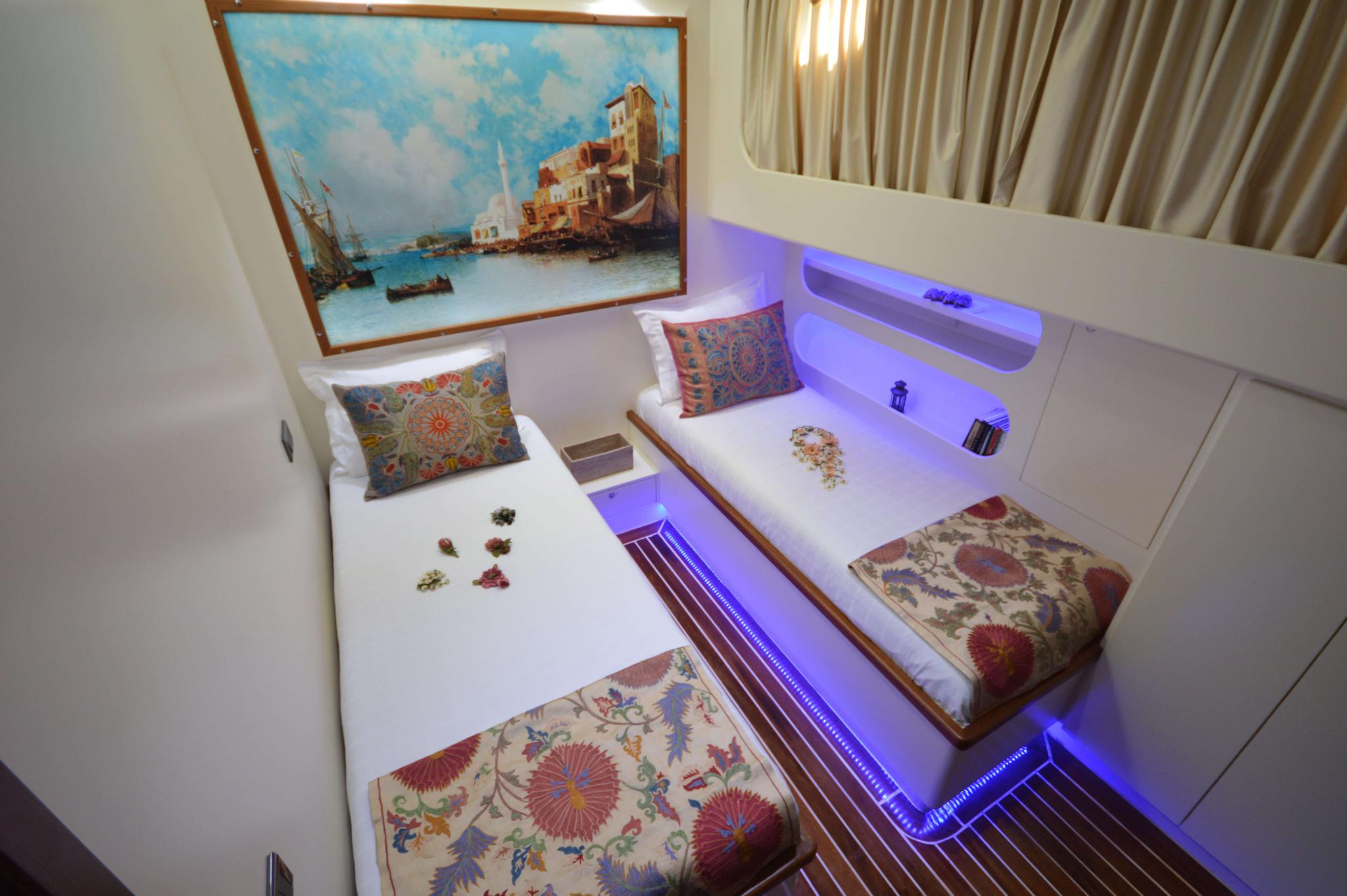 yacht twin cabin with white beds, decorative pillows, LED lighting and maritime artwork