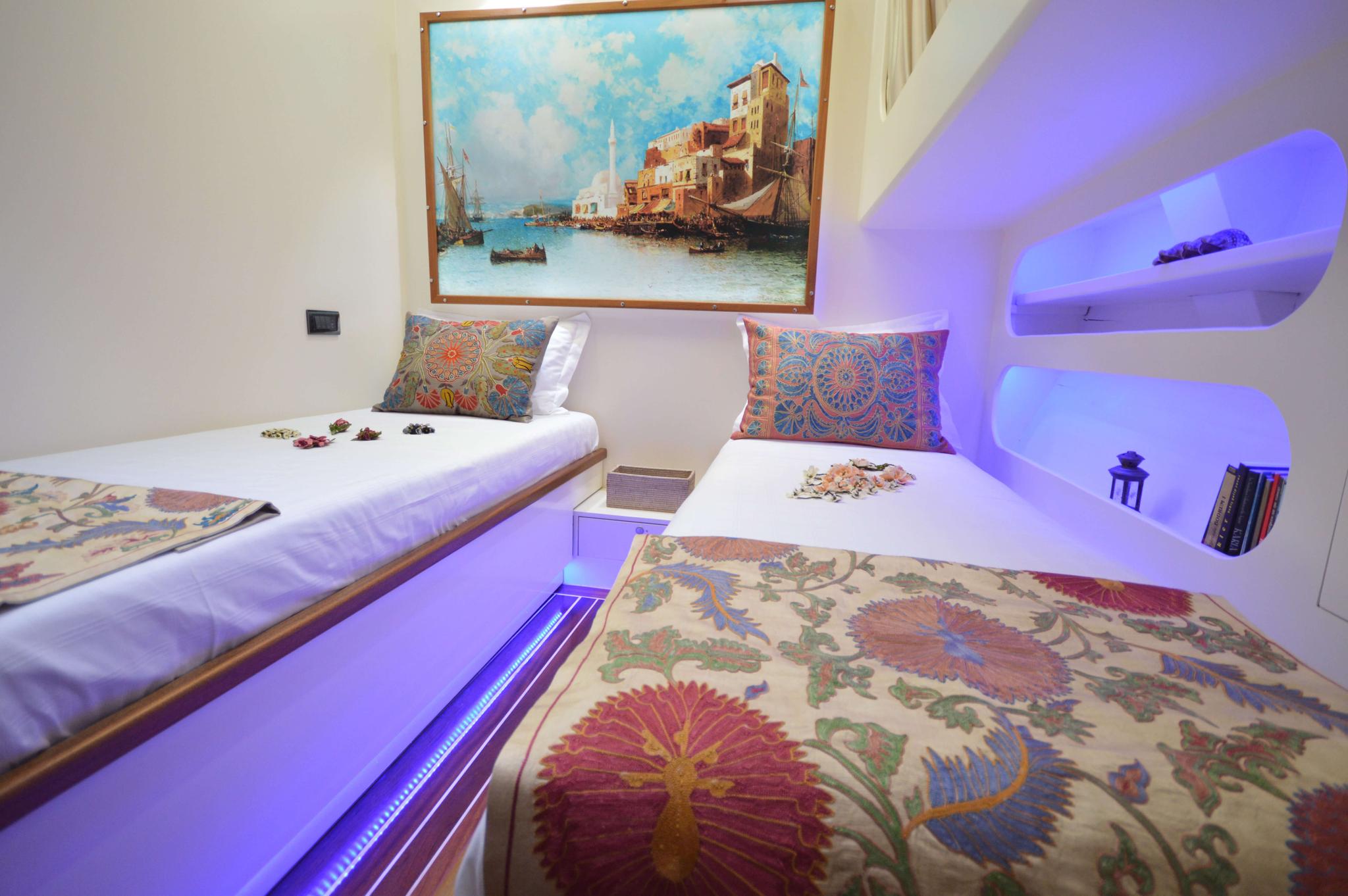 yacht twin bed cabin with colorful paisley pillows and Mediterranean coastal artwork