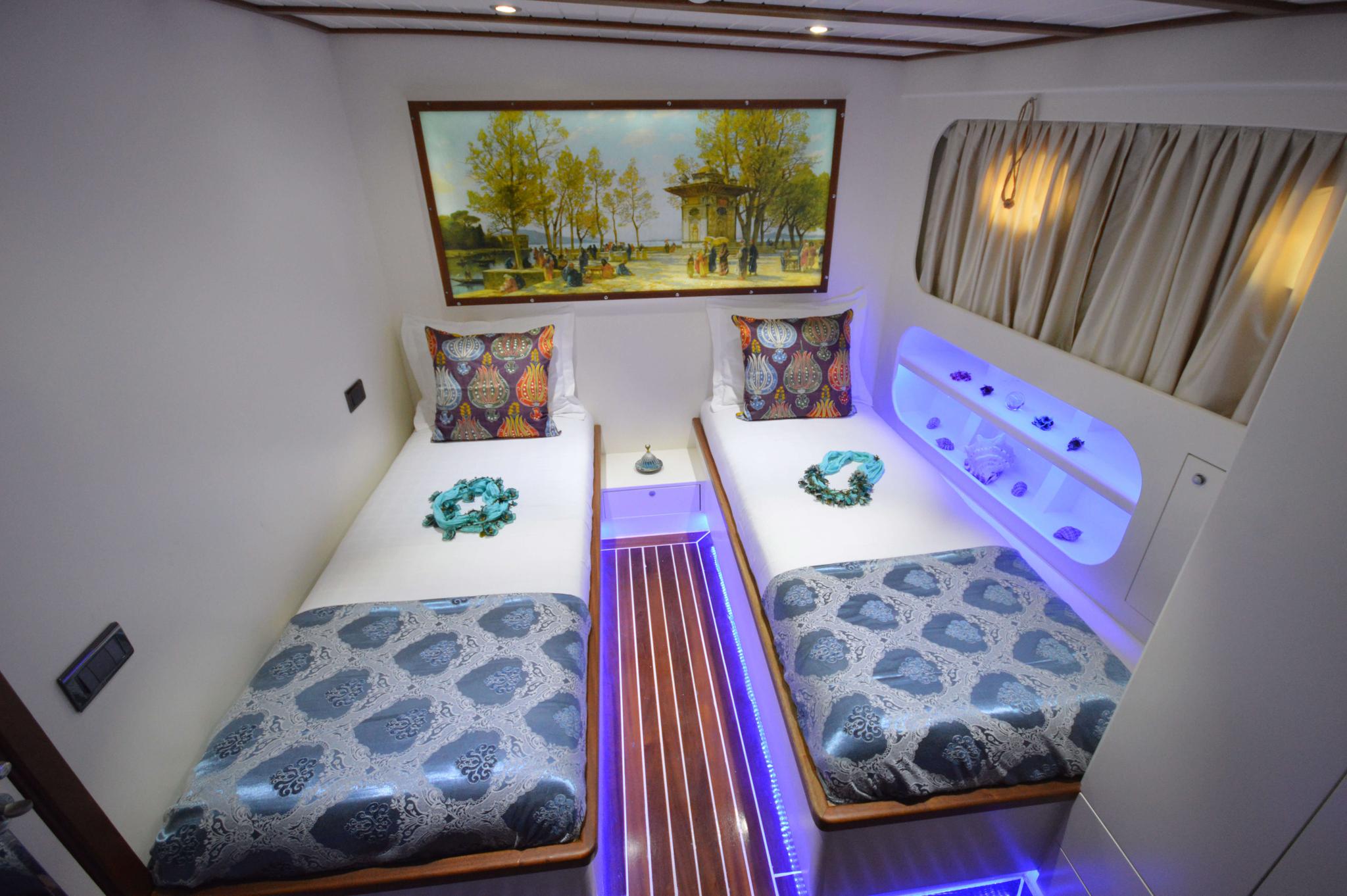 yacht twin bed cabin with patterned bedding, decorative pillows and blue LED accent lighting