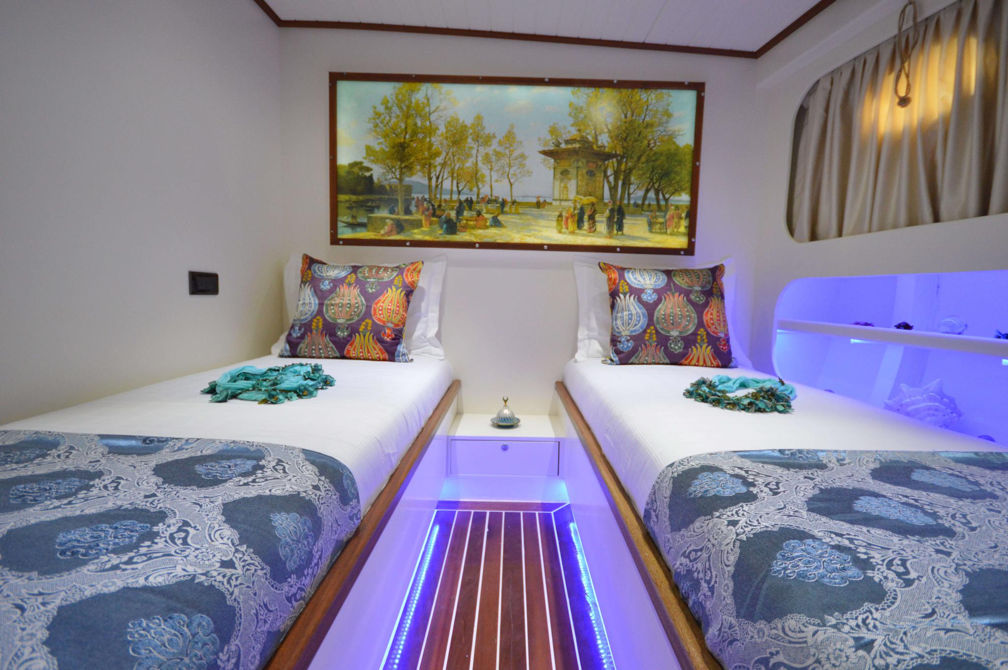 yacht twin cabin with two single beds, decorative pillows and purple LED lighting