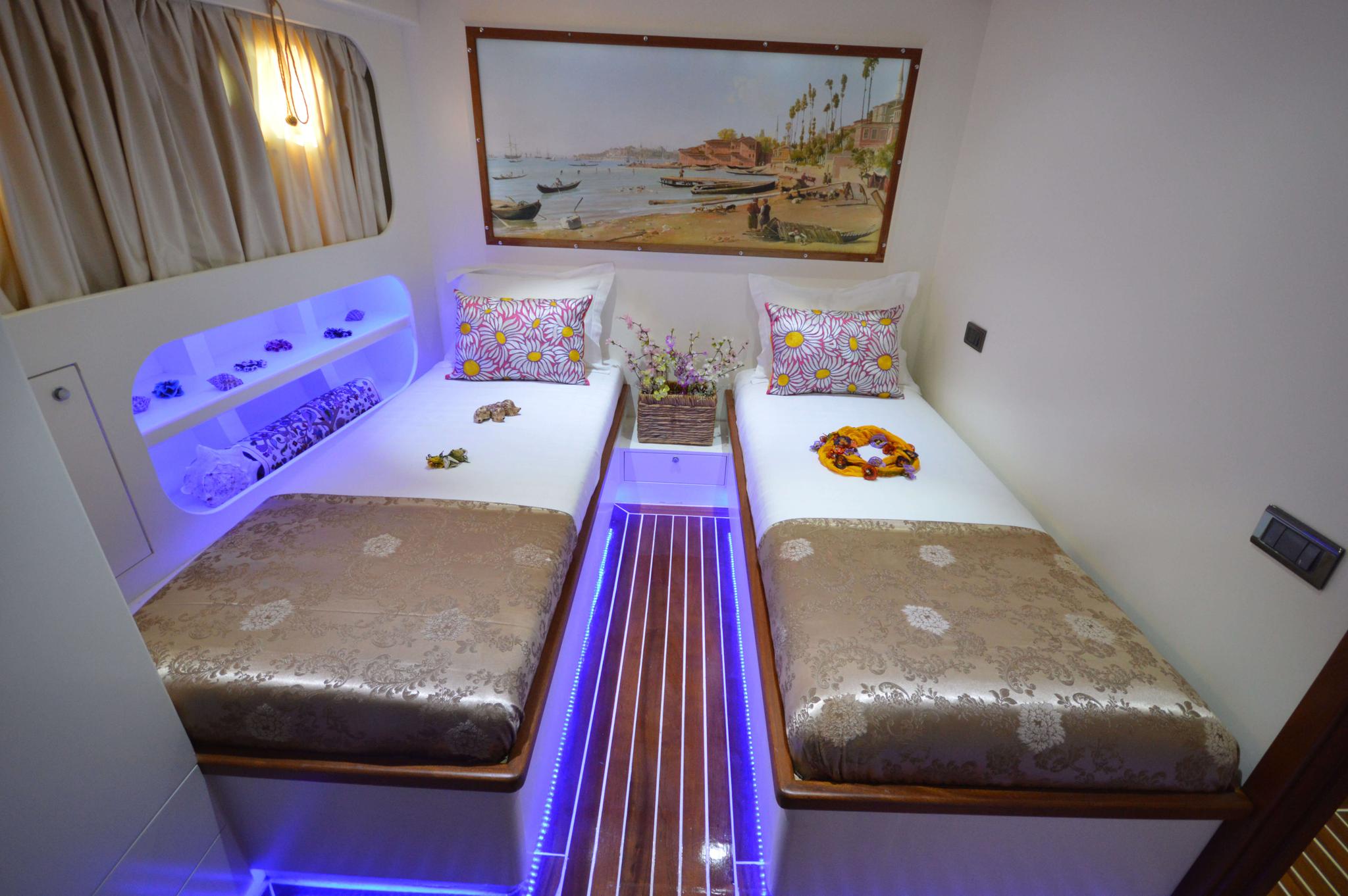 yacht twin cabin with two single beds, blue LED lighting, coastal painting and floral pillows
