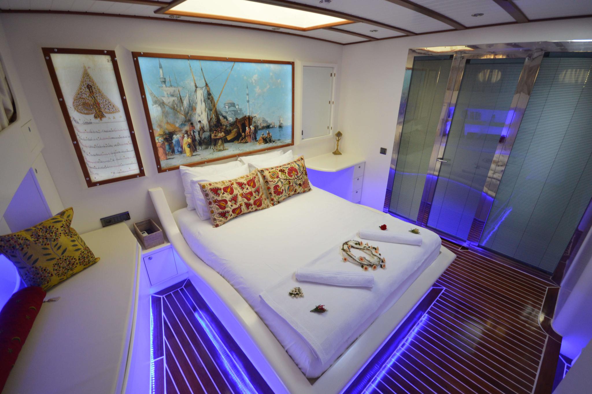 yacht master cabin with white king bed, decorative pillows, blue LED accent lighting and maritime artwork