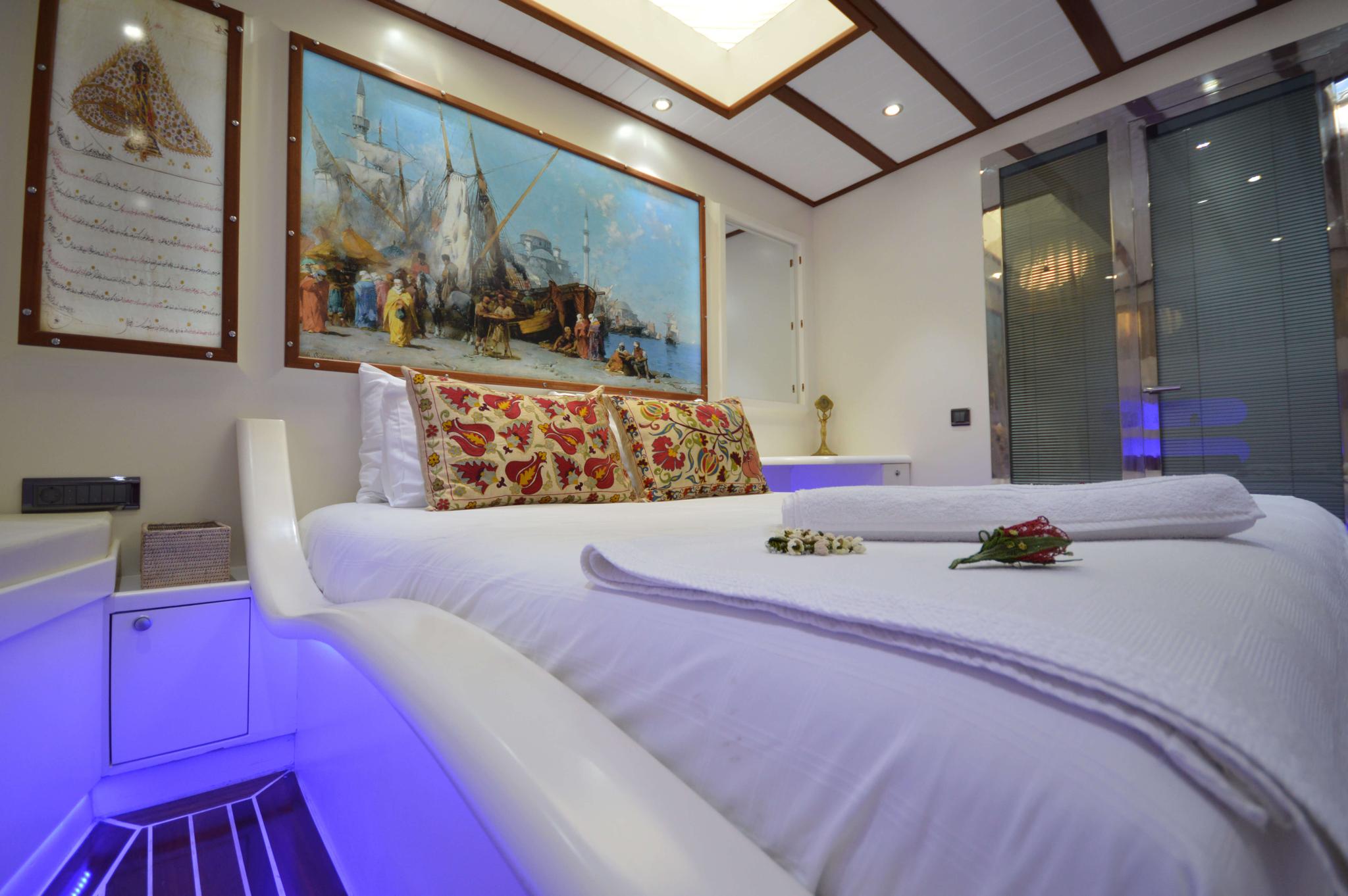 yacht cabin interior with white bedding, traditional paisley cushions, maritime artwork and blue ambient lighting