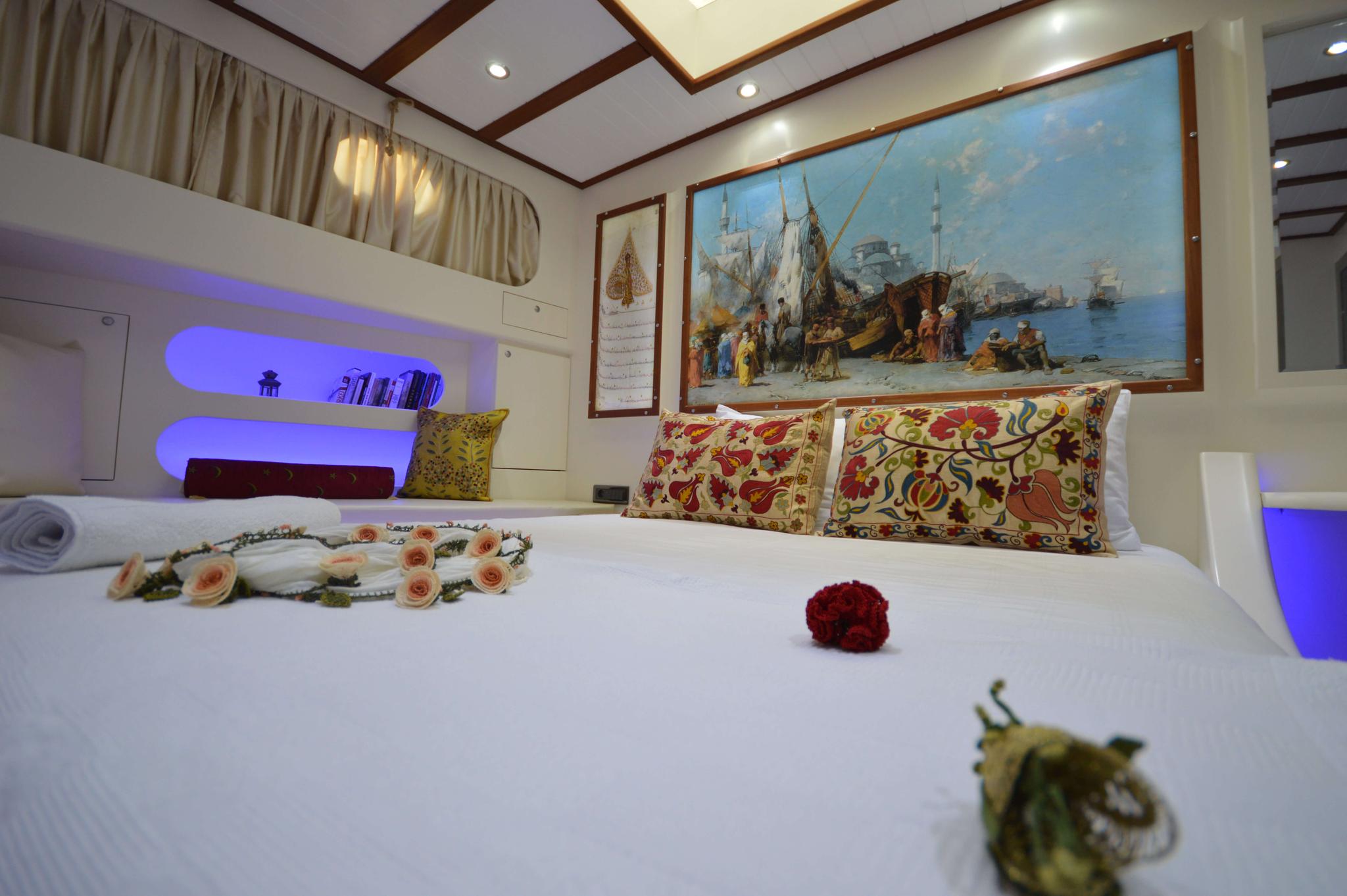 yacht guest cabin featuring white bedding, ornate decorative pillows, built-in shelving with blue LED lighting