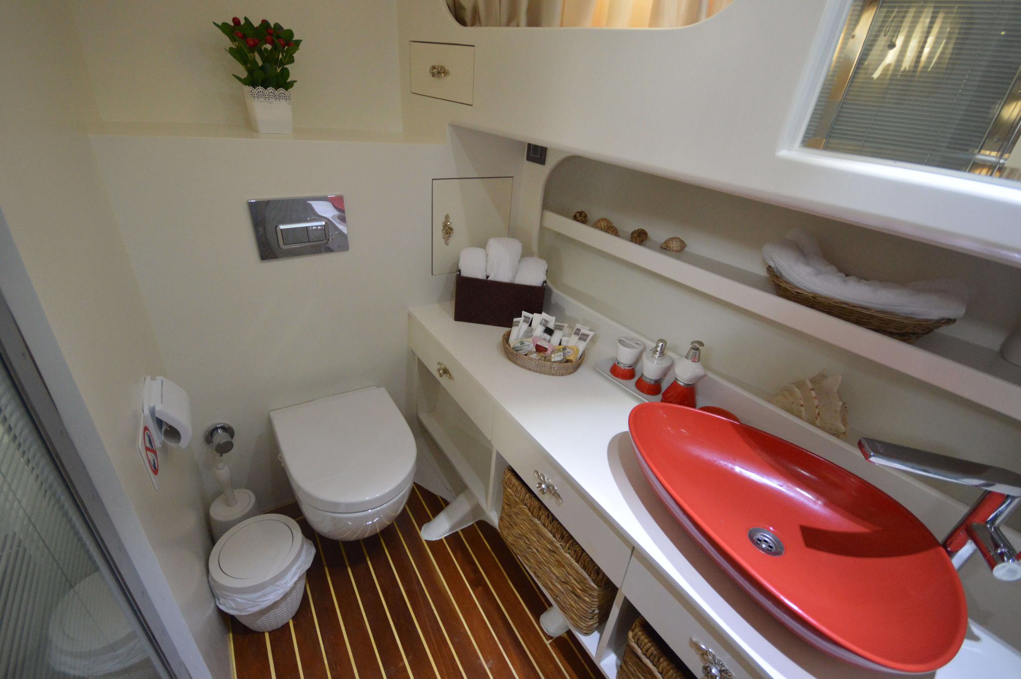 yacht bathroom with red oval vessel sink, white vanity, toilet and bathtub