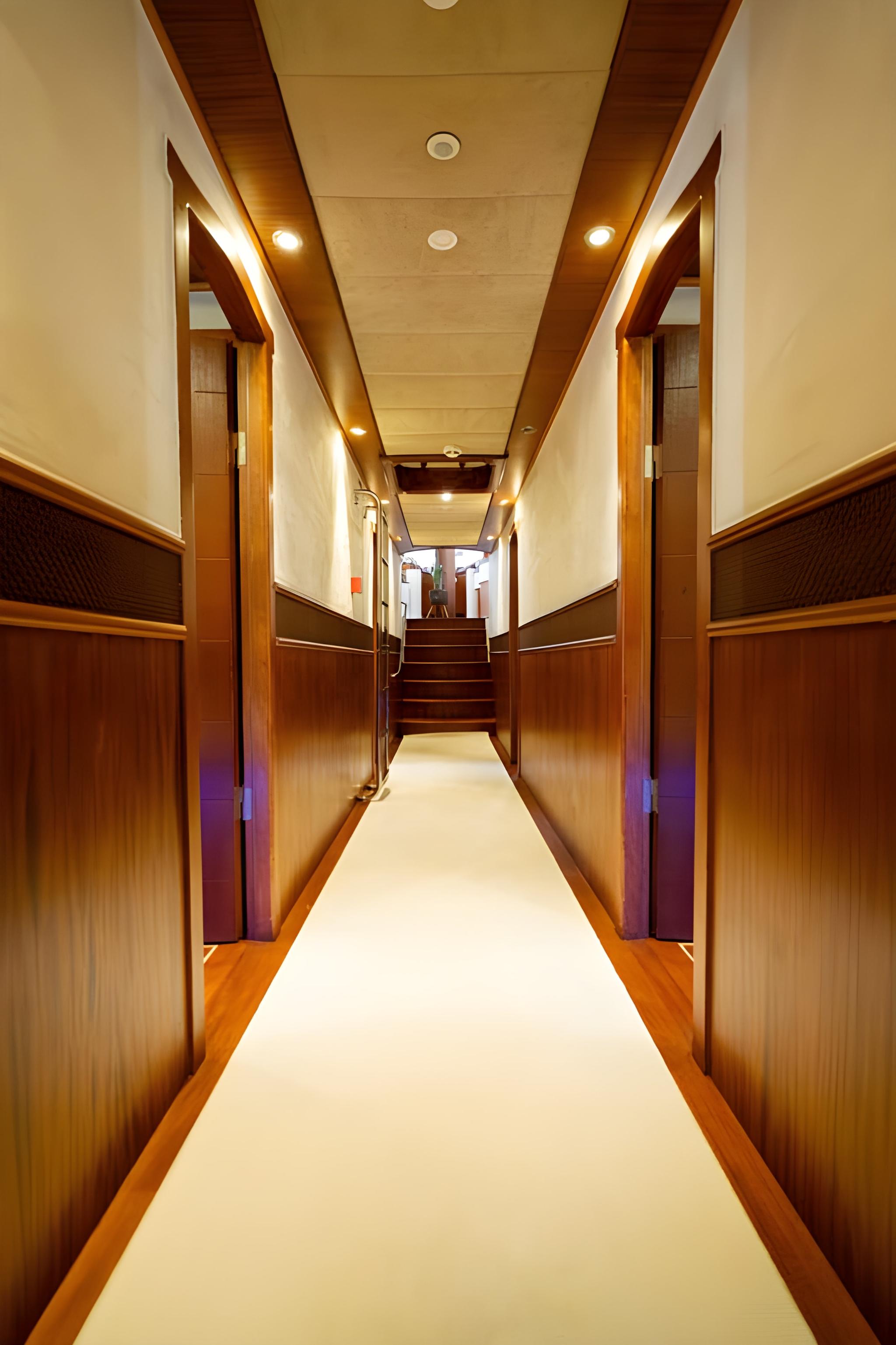 luxury yacht interior corridor with warm wood paneling, recessed lighting, and multiple cabin doors leading to guest quarters