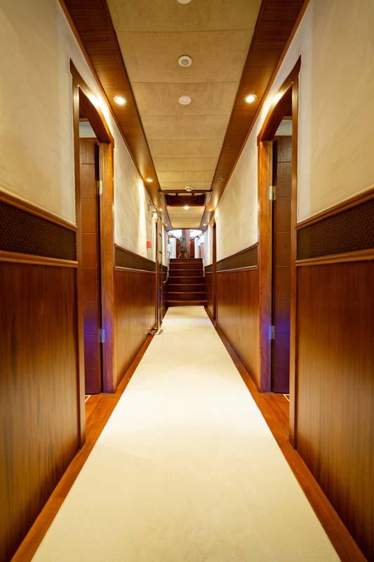 luxury yacht interior corridor with warm wood paneling, recessed lighting, and multiple cabin doors leading to guest quarters