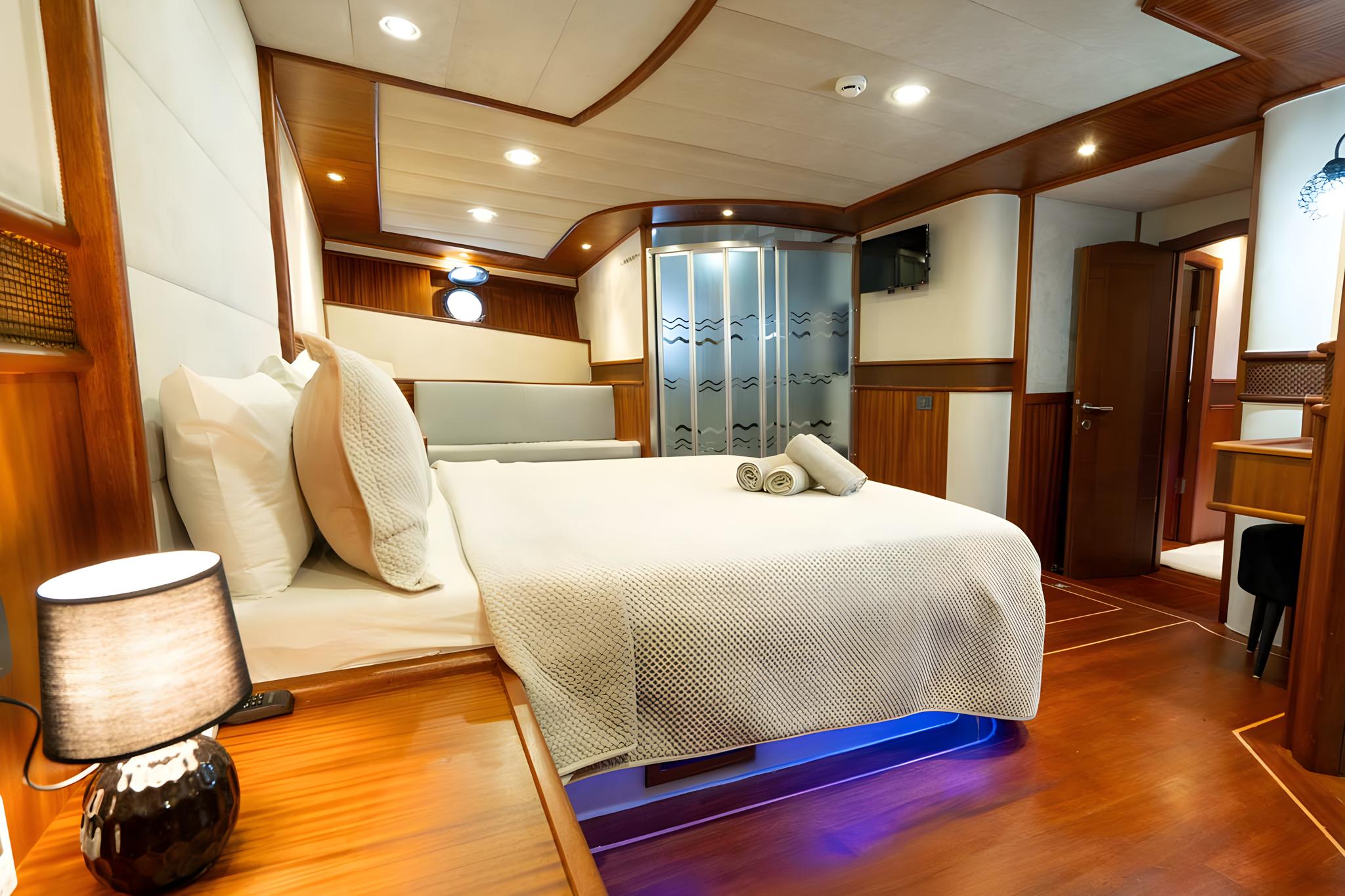 Yacht master cabin with white bedding, wood paneling, ensuite shower, and blue LED lighting