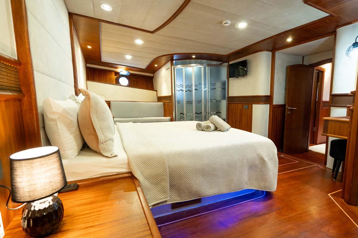 Yacht master cabin with white bedding, wood paneling, ensuite shower, and blue LED lighting