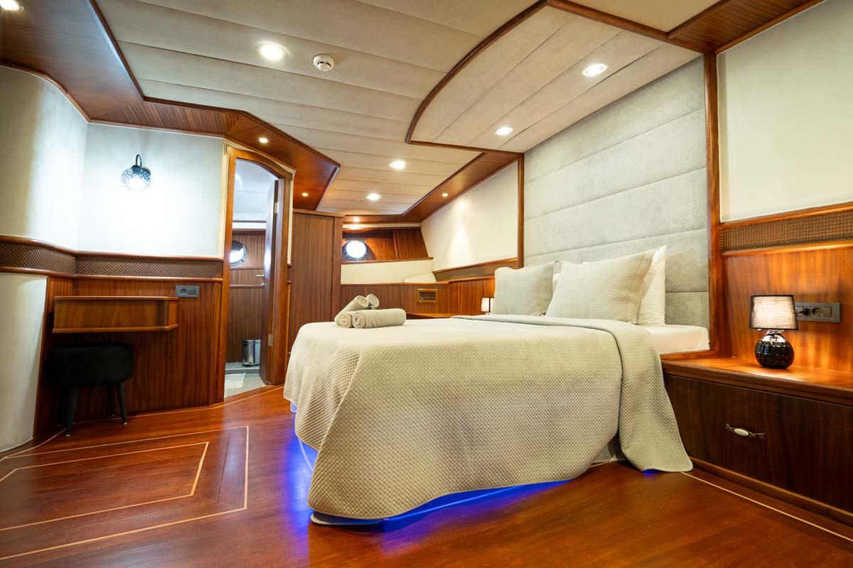 luxury yacht master cabin featuring king bed with beige linens, wood paneling, recessed lighting and ensuite doorway