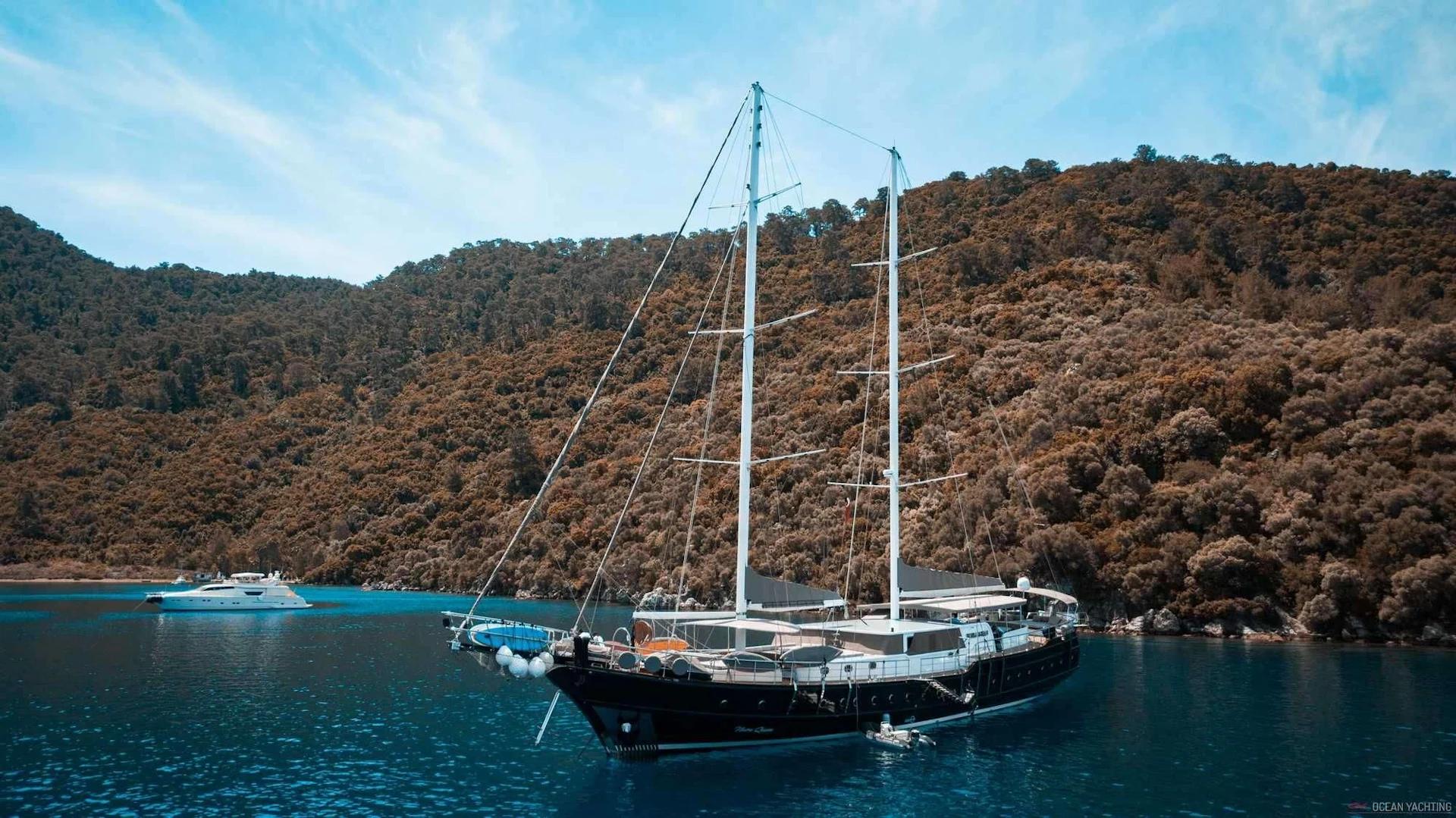 Traditional wooden gulet yacht with two masts anchored in pristine turquoise bay surrounded by forested hills