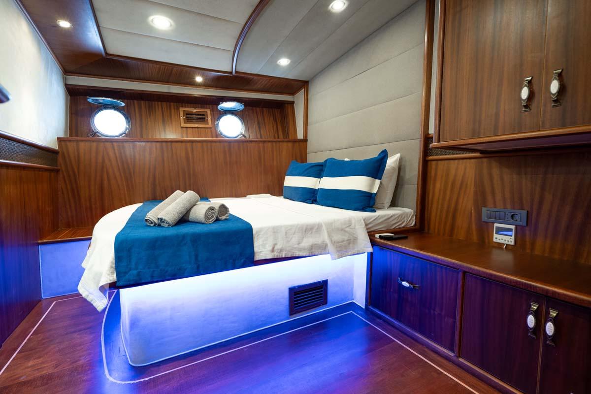 yacht cabin interior with double bed, blue accent lighting, portholes, and wooden cabinetry