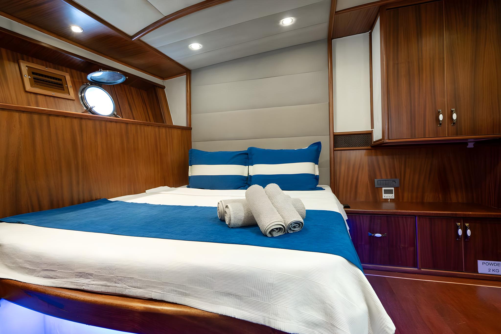 yacht cabin interior with double bed, blue bedding, wood paneling and portholes