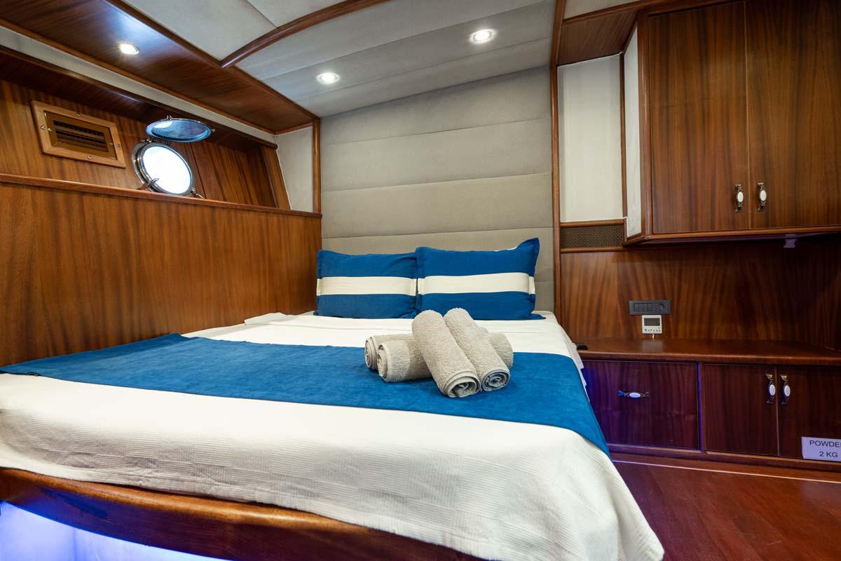 yacht cabin interior with double bed, blue bedding, wood paneling and portholes