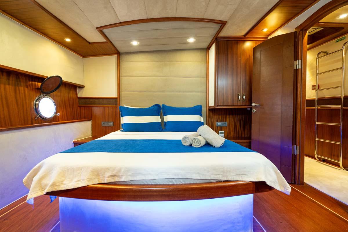 yacht cabin interior with double bed, blue accent lighting, porthole window and wooden finishes