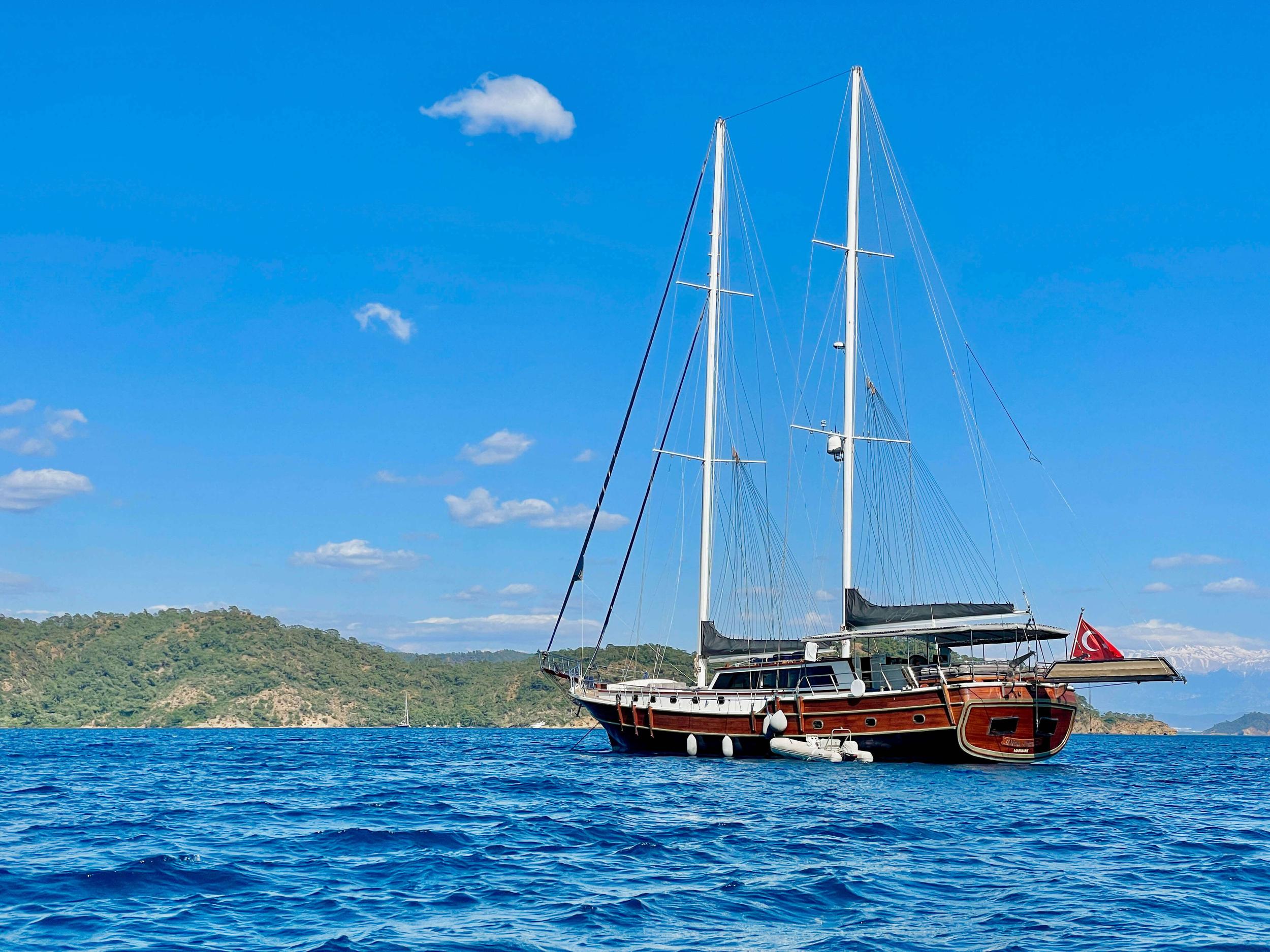 Traditional wooden gulet with two masts sailing in Mediterranean waters near forested coastline