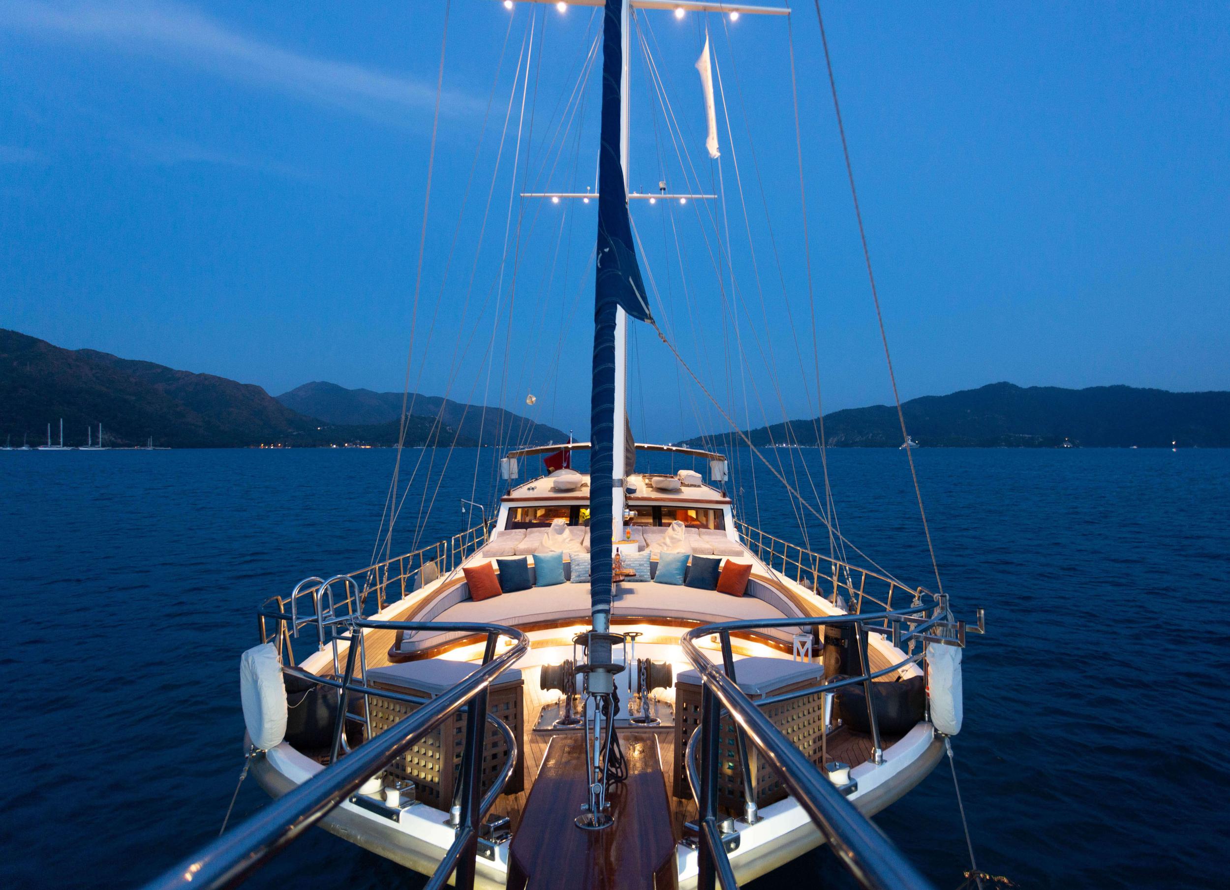 gulet bow deck with curved seating cushions and decorative pillows at twilight
