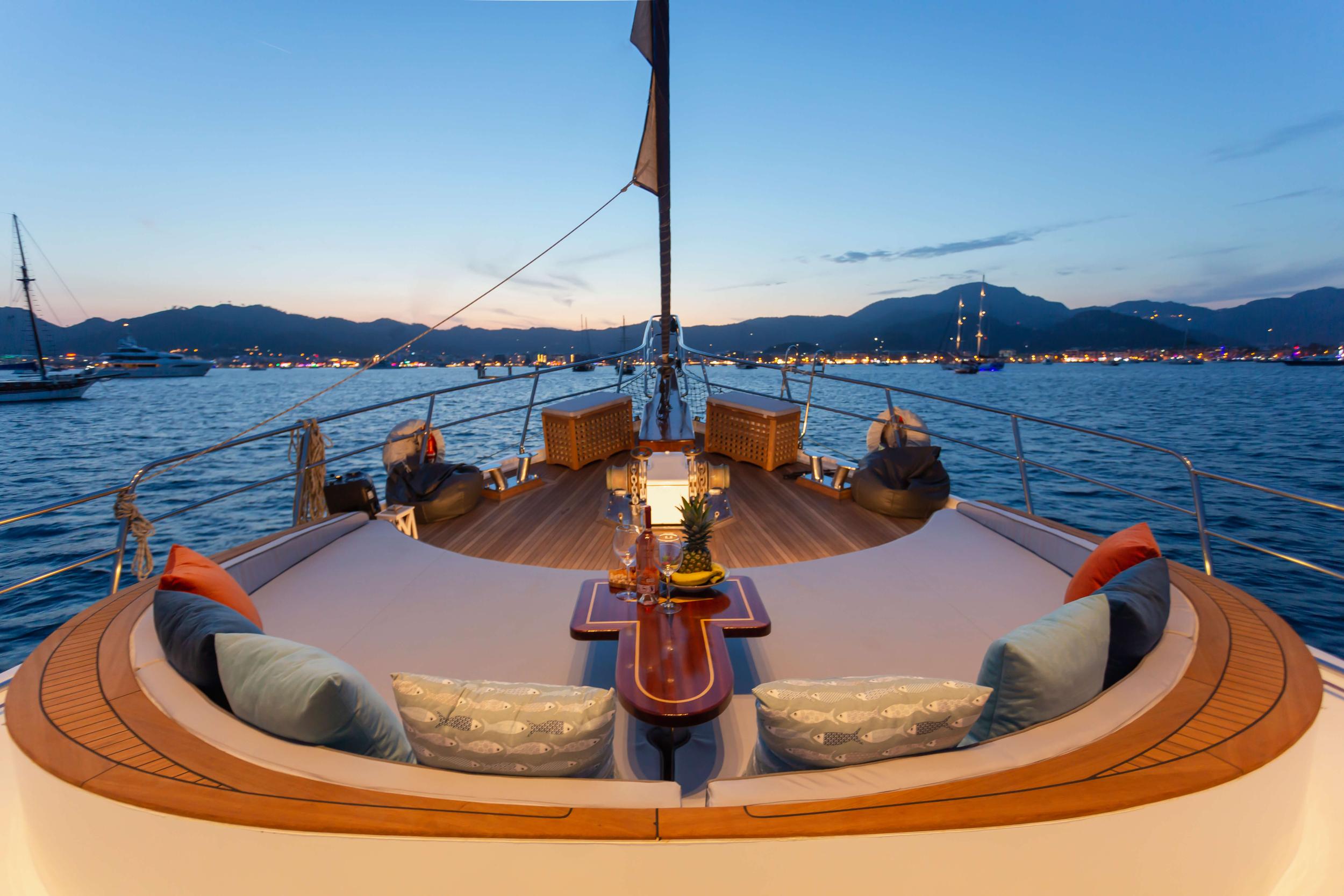 gulet bow deck with curved cushioned seating and wooden table at sunset
