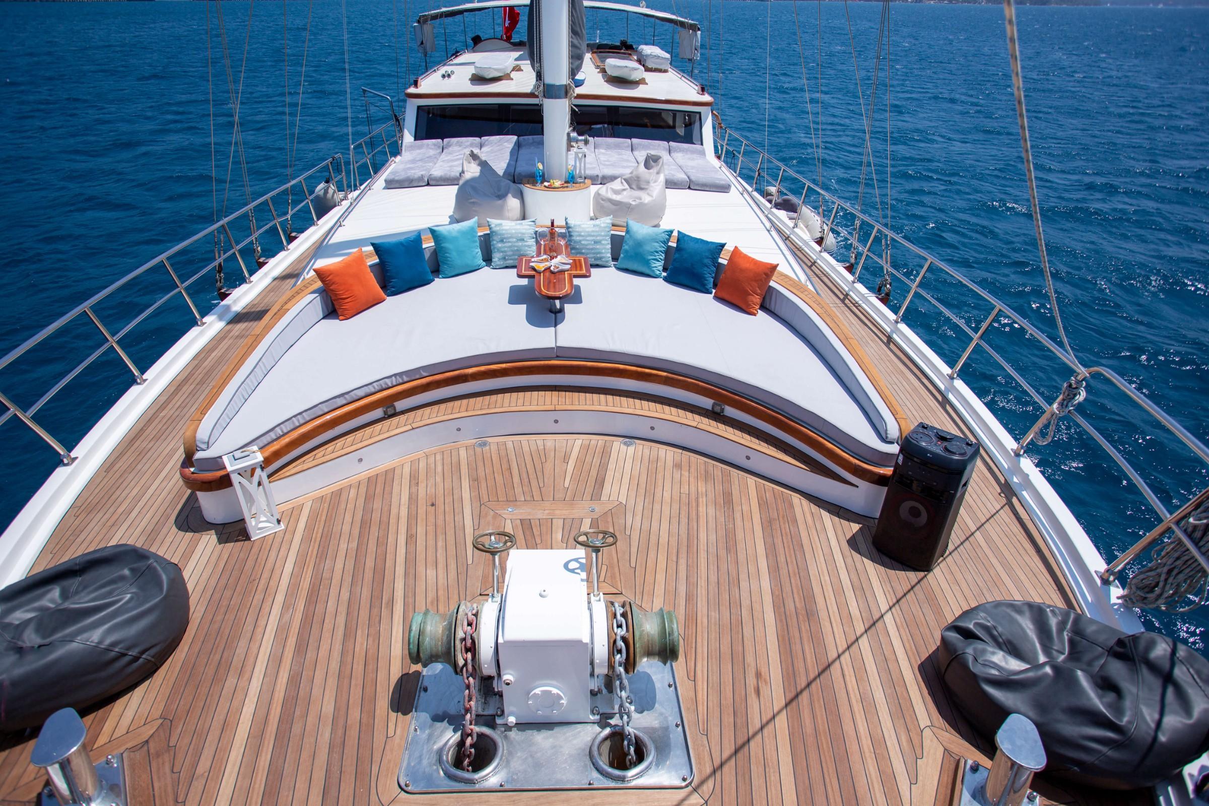 Gulet bow deck with curved white banquette seating, colorful cushions, teak decking and windlass