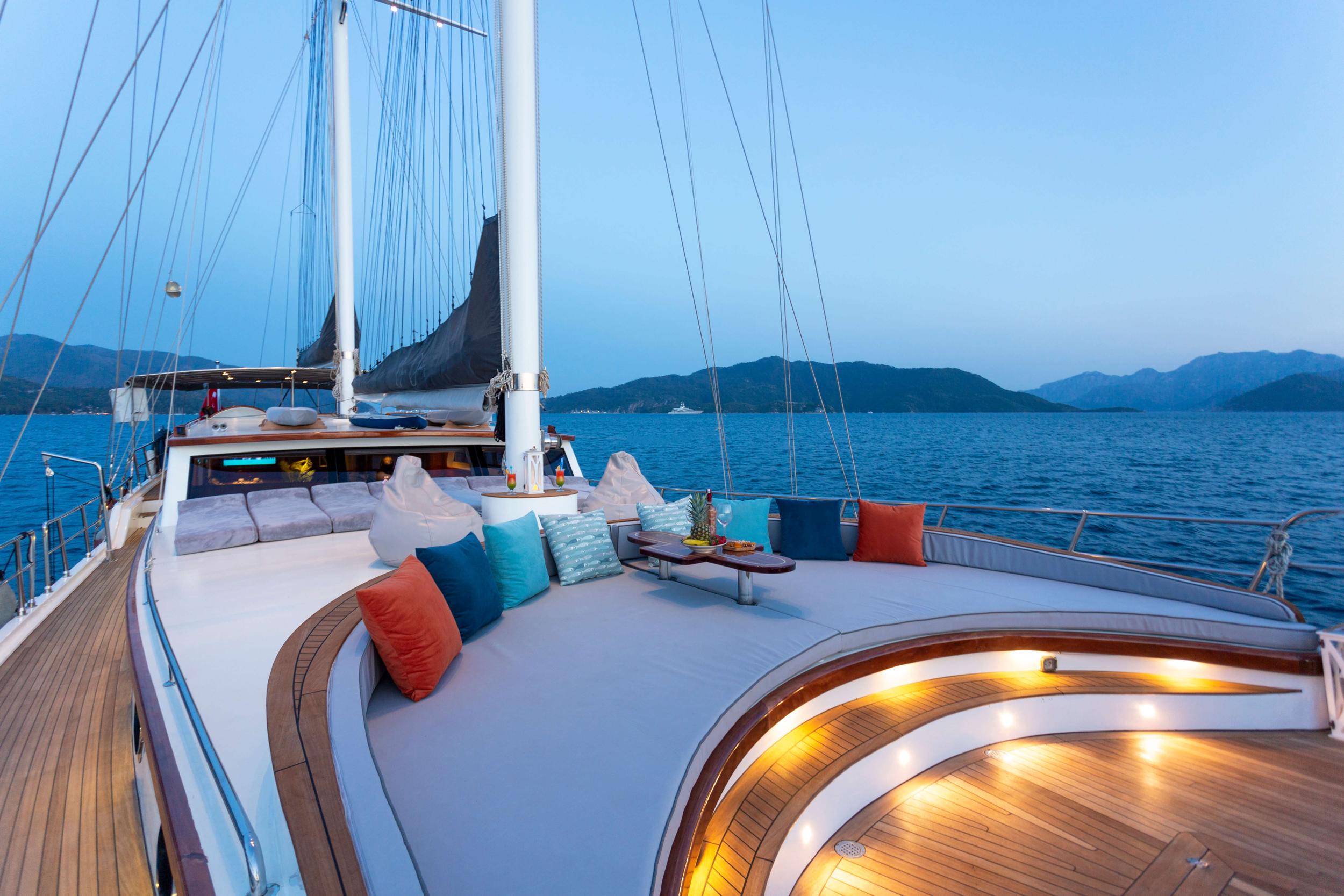 gulet forward deck curved seating area with colorful cushions and ambient lighting at dusk