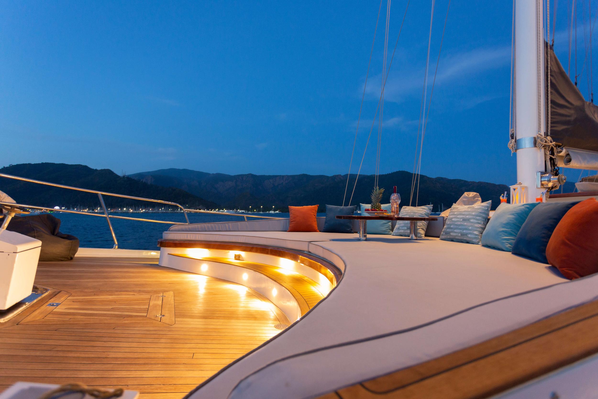 yacht aft deck with curved white seating, LED lighting, and mountain coastline at dusk