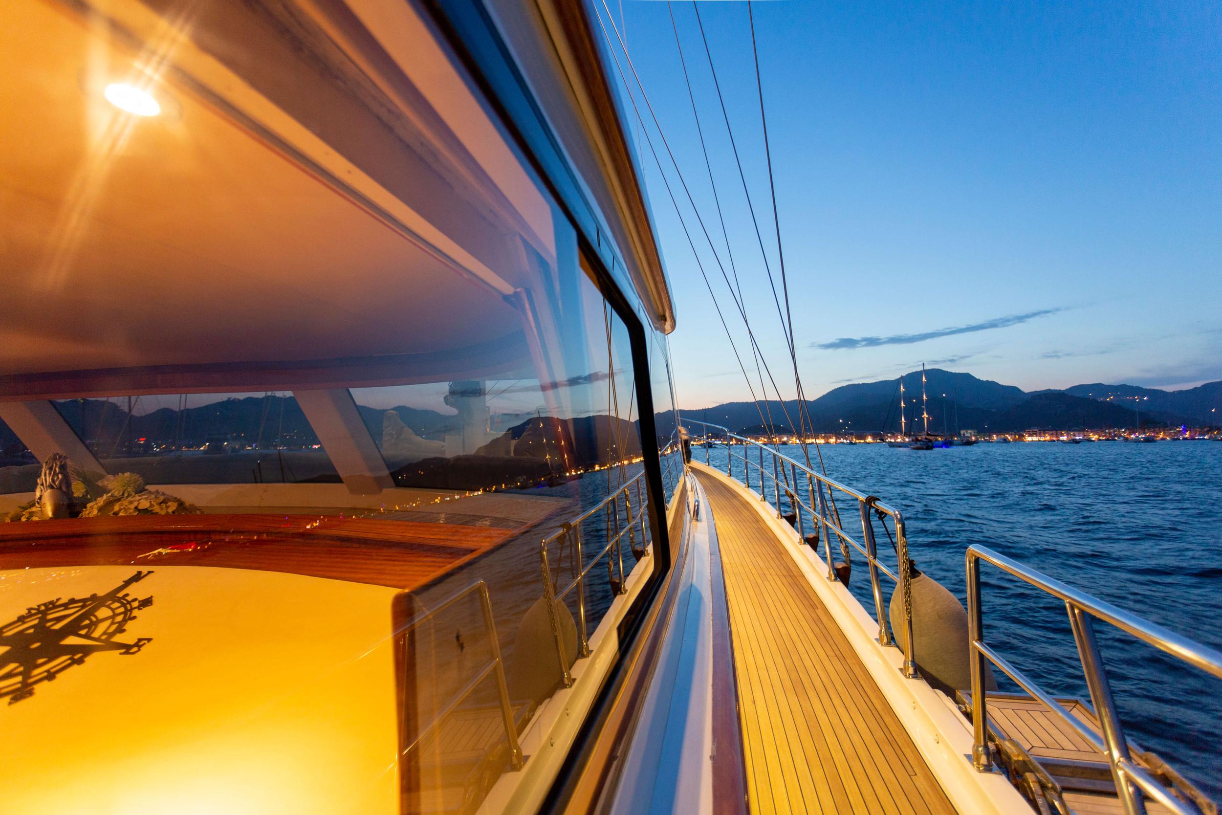 yacht side deck with teak flooring and stainless steel railings at twilight overlooking coastal mountains