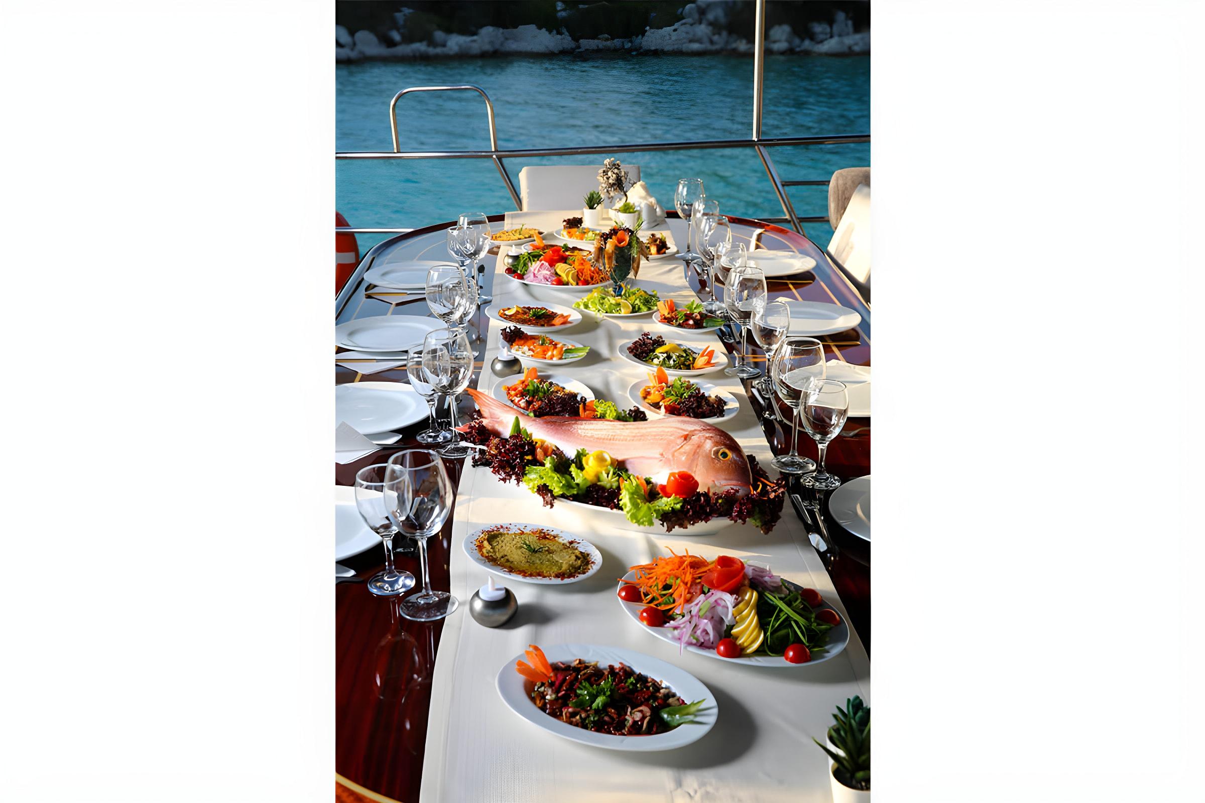 yacht dining table with whole fish, Mediterranean dishes, wine glasses and formal place settings