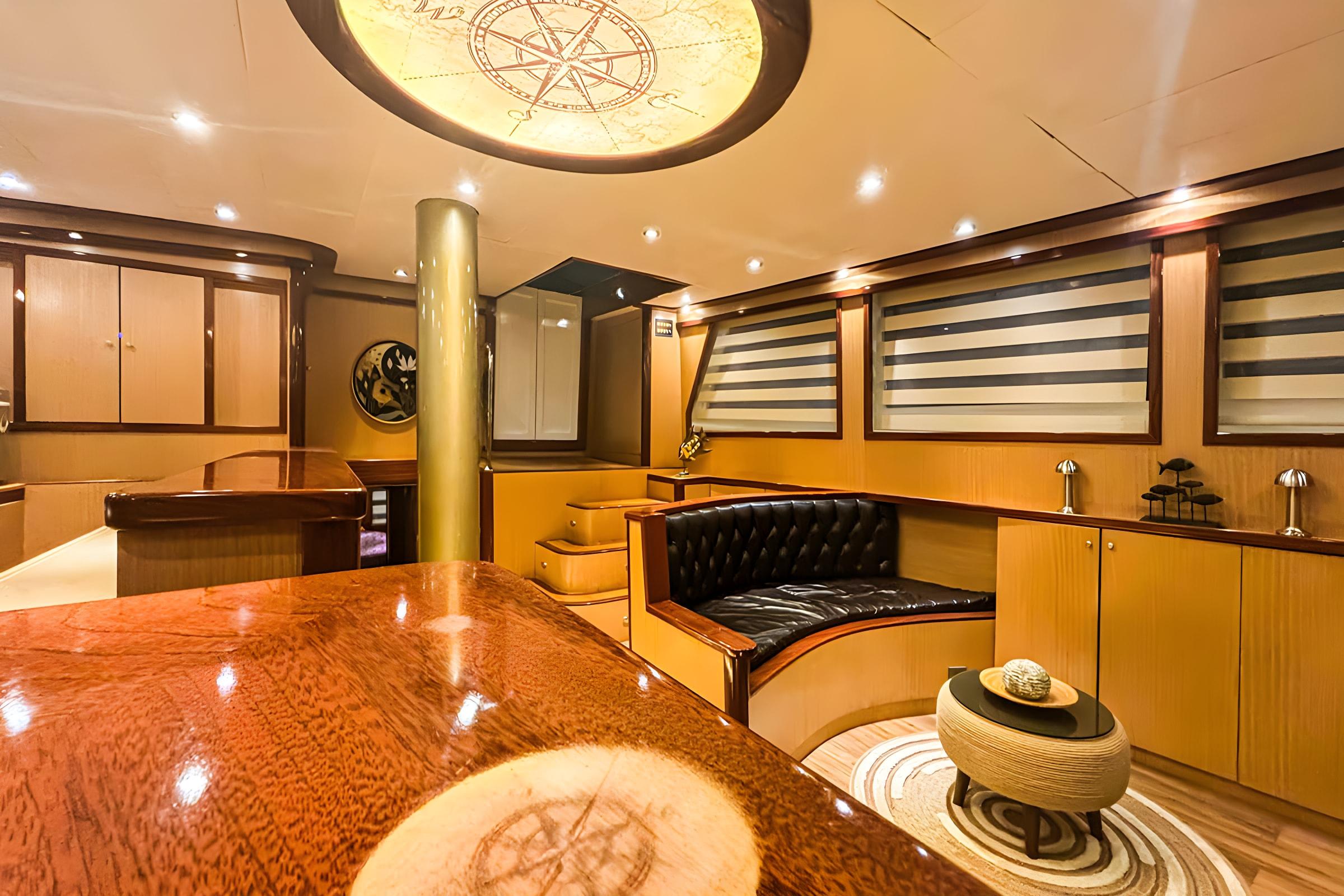 luxury yacht main salon with curved black leather seating, polished wood table and compass ceiling feature