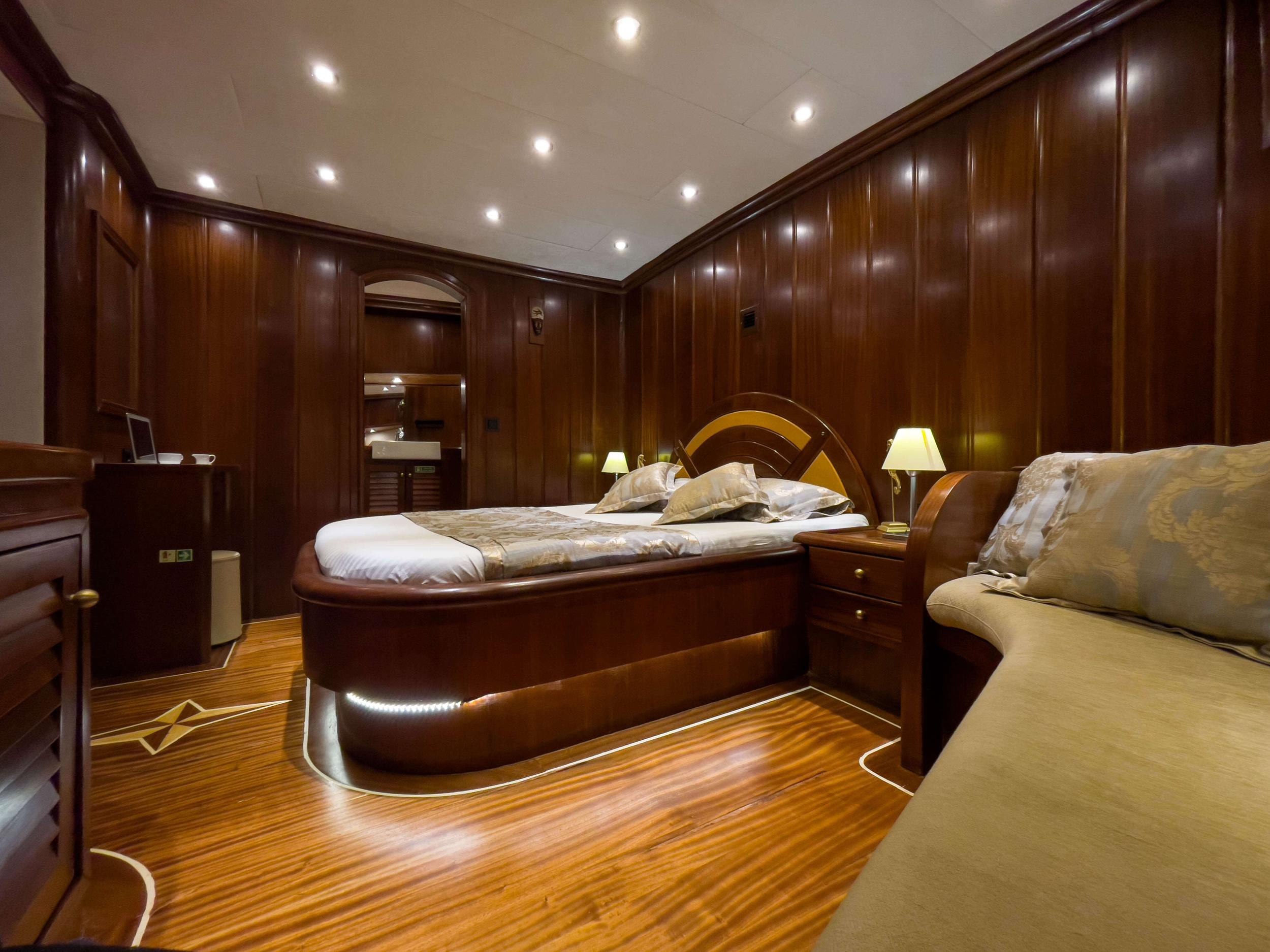 luxury yacht master cabin with curved mahogany bed, wood paneling and ensuite bathroom