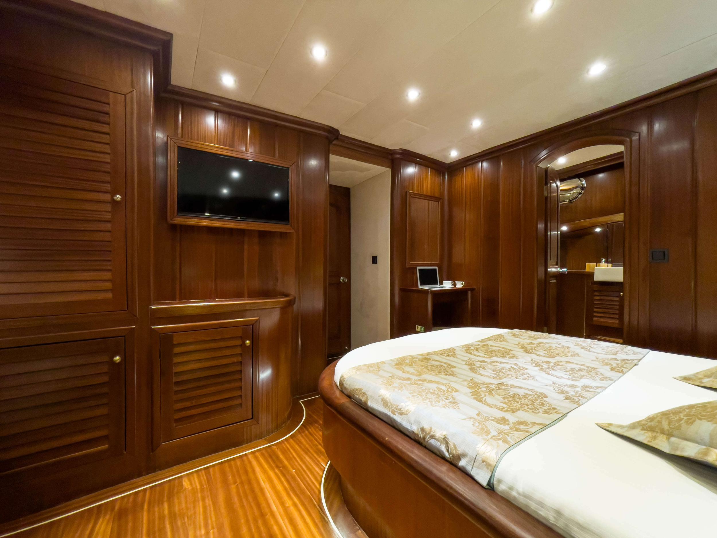 yacht cabin with double bed, wall-mounted TV, mahogany paneling and en-suite bathroom entrance