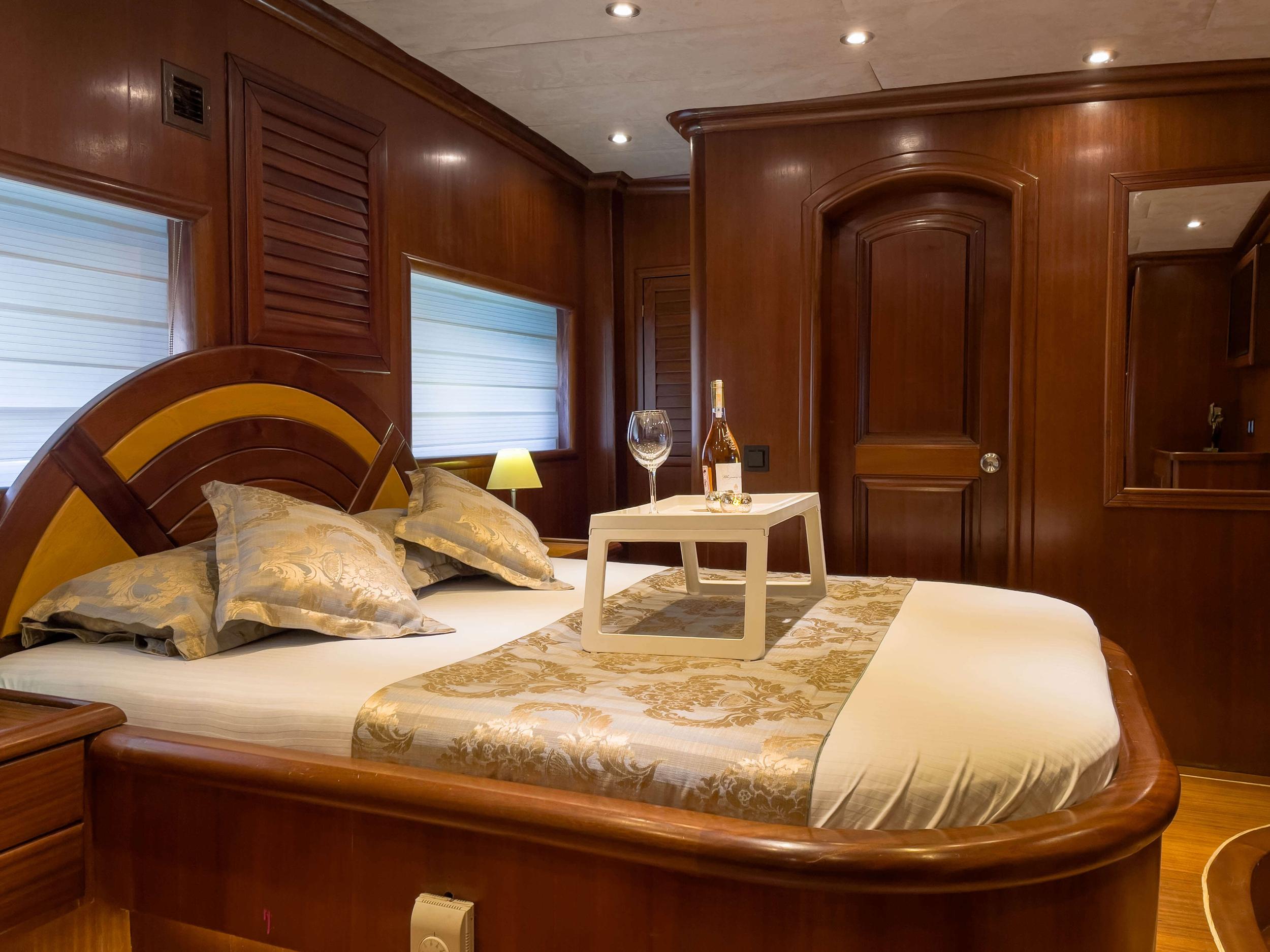 luxury yacht cabin featuring curved headboard double bed with gold accents and rich wood paneling