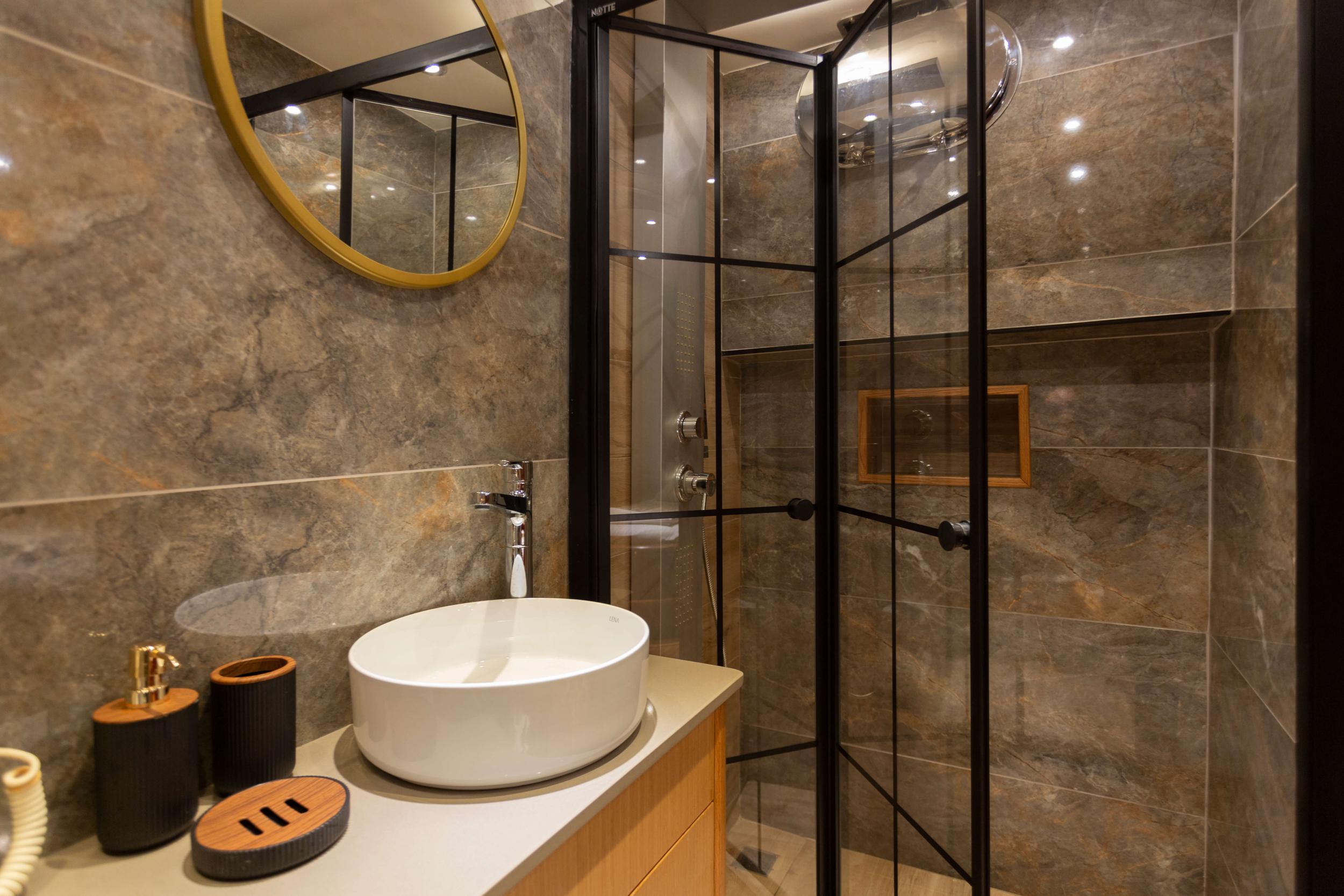 luxury yacht bathroom with round white basin, marble walls, black-framed glass shower enclosure