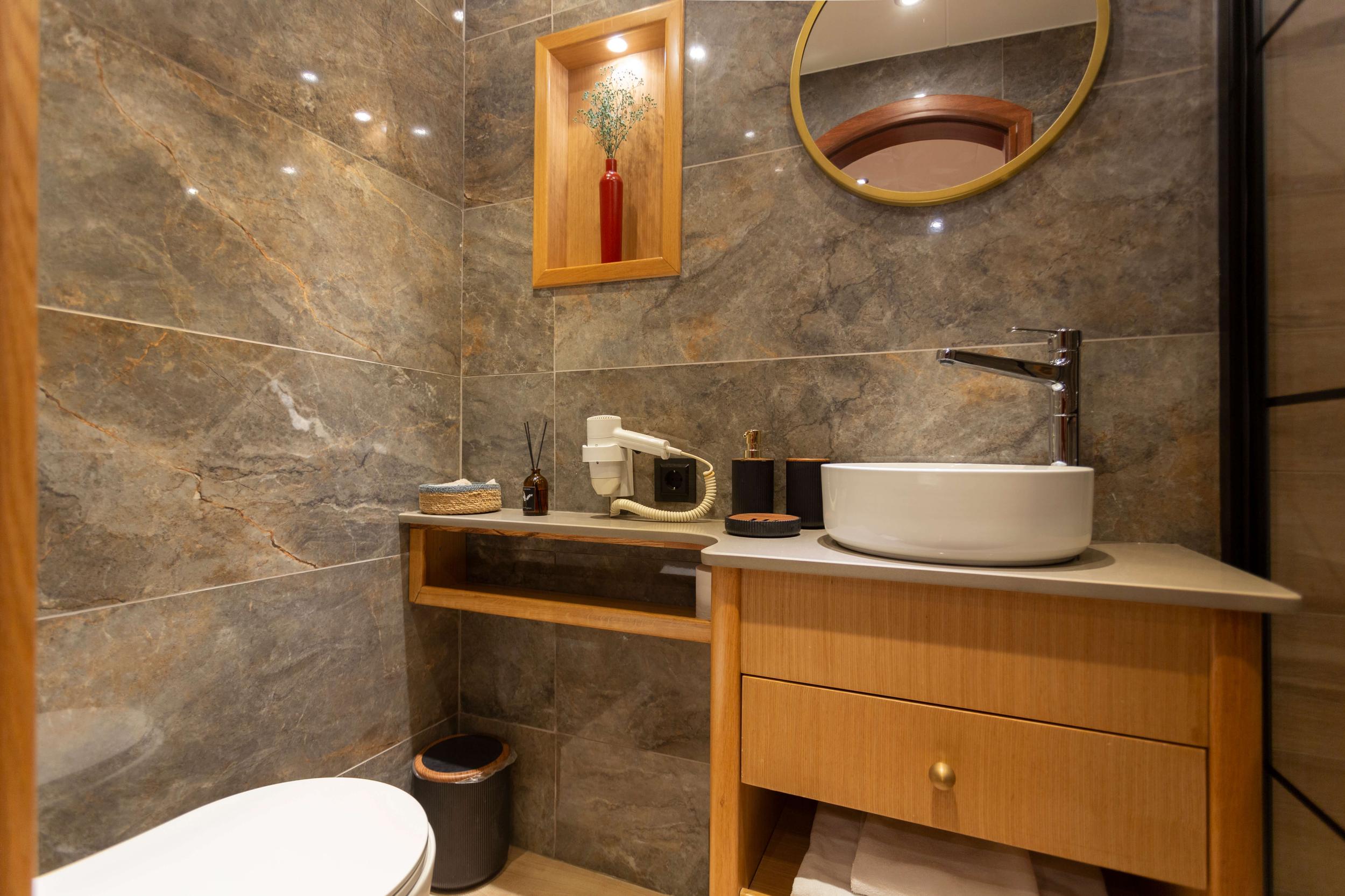 luxury yacht bathroom featuring marble walls, white vessel sink, and wooden vanity