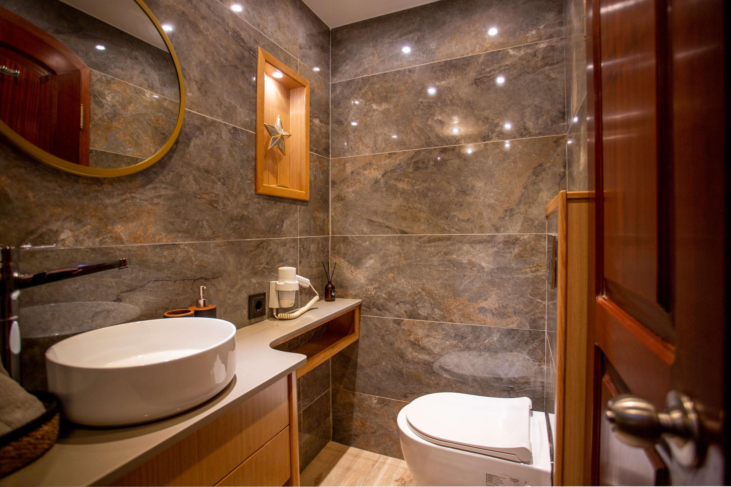 yacht bathroom featuring gray marble walls, white vessel sink, and glass shower enclosure
