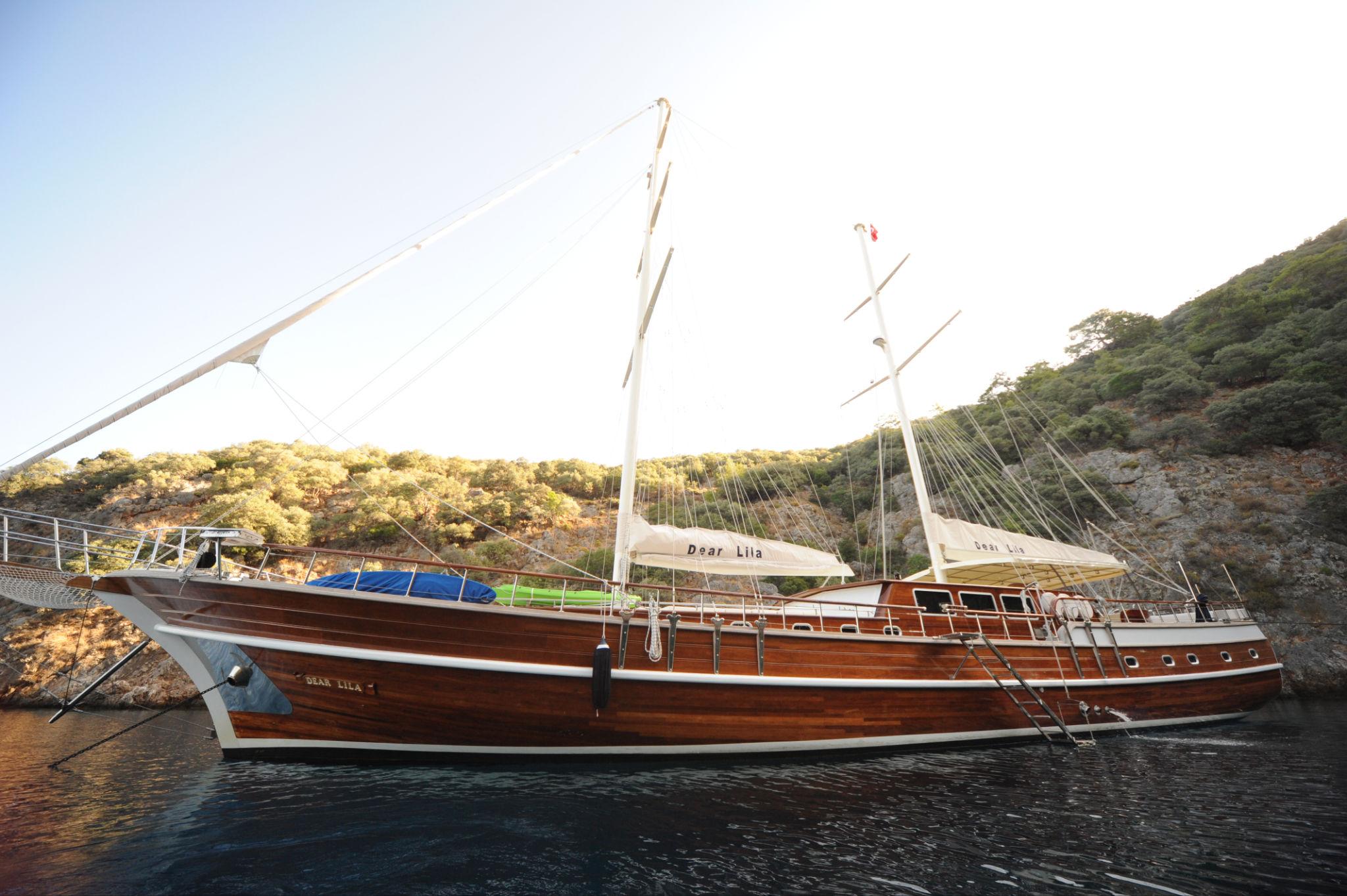 wooden gulet Dear Lila at anchor in rocky Mediterranean cove with forested hills