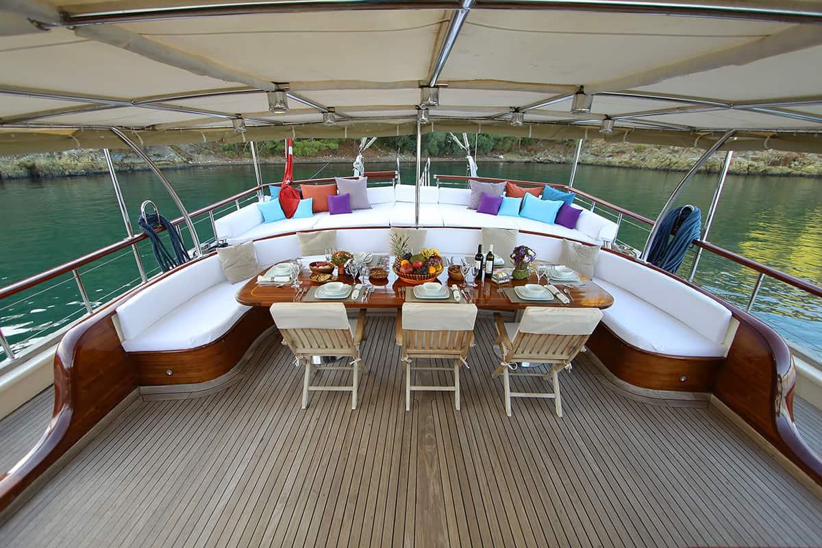 yacht aft deck dining table set with food, wine bottles and place settings under awning