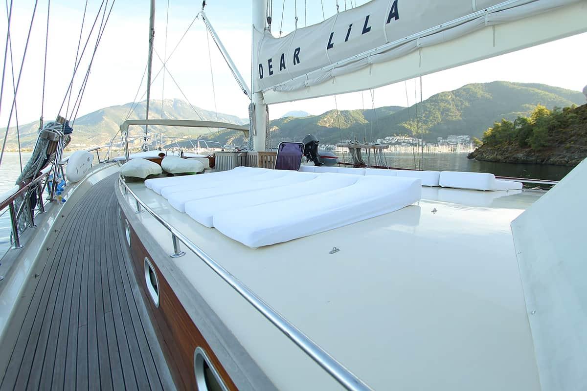 Gulet forward deck with large white sunbathing cushions and teak decking