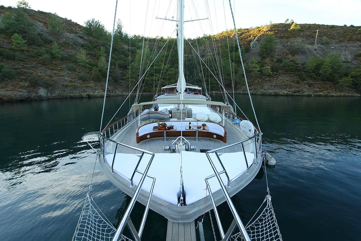 white sailing gulet with two masts anchored in calm turquoise cove surrounded by hills