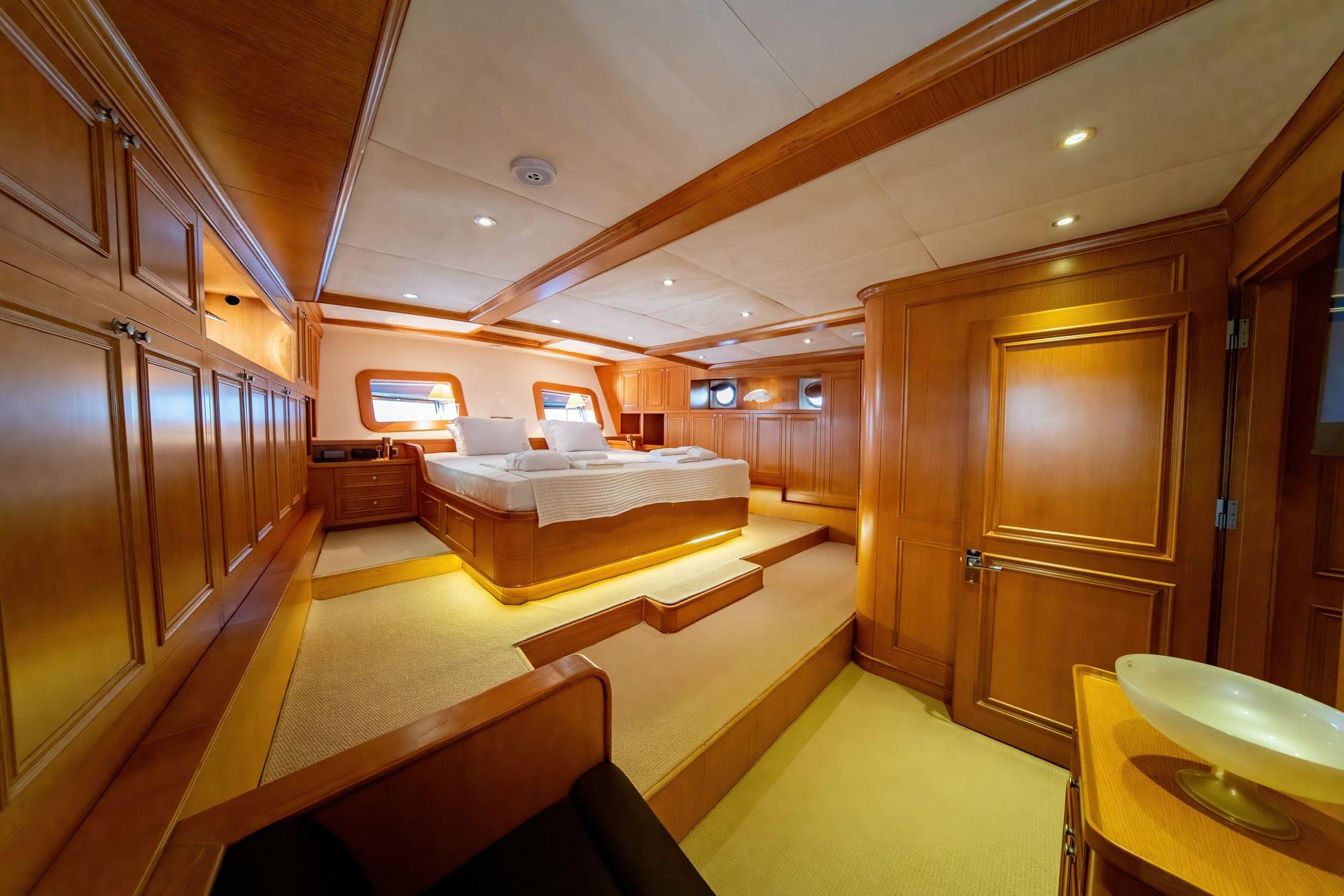 luxury yacht master cabin featuring king bed, wooden paneling, porthole windows and marble basin