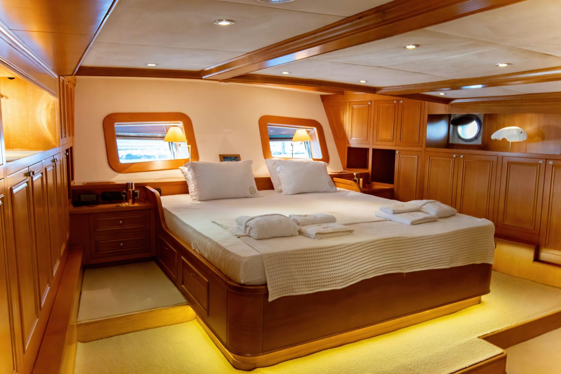 luxury yacht master cabin featuring king bed with white linens and wooden portholes
