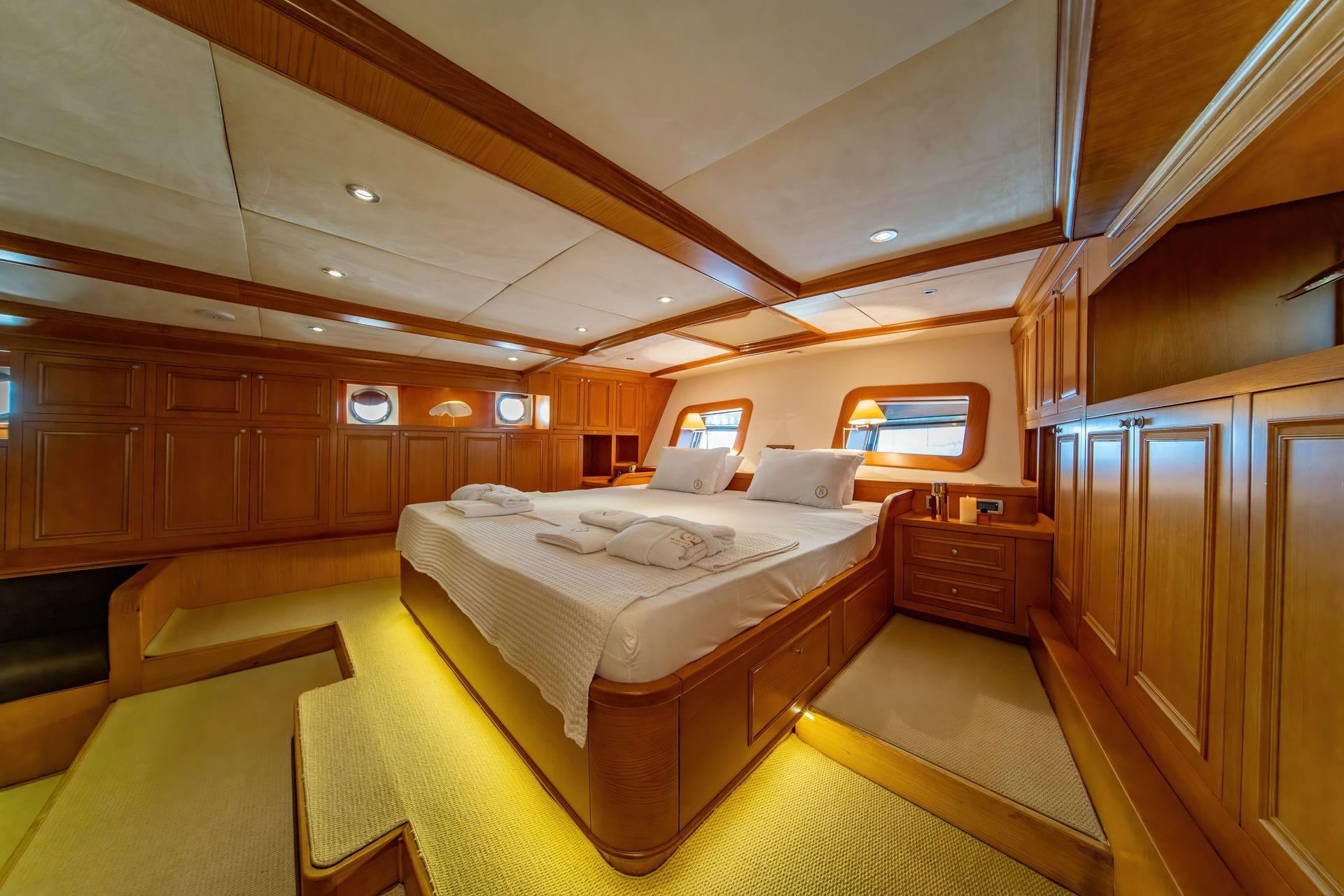 yacht cabin interior with double bed, white linens, wood paneling and portholes