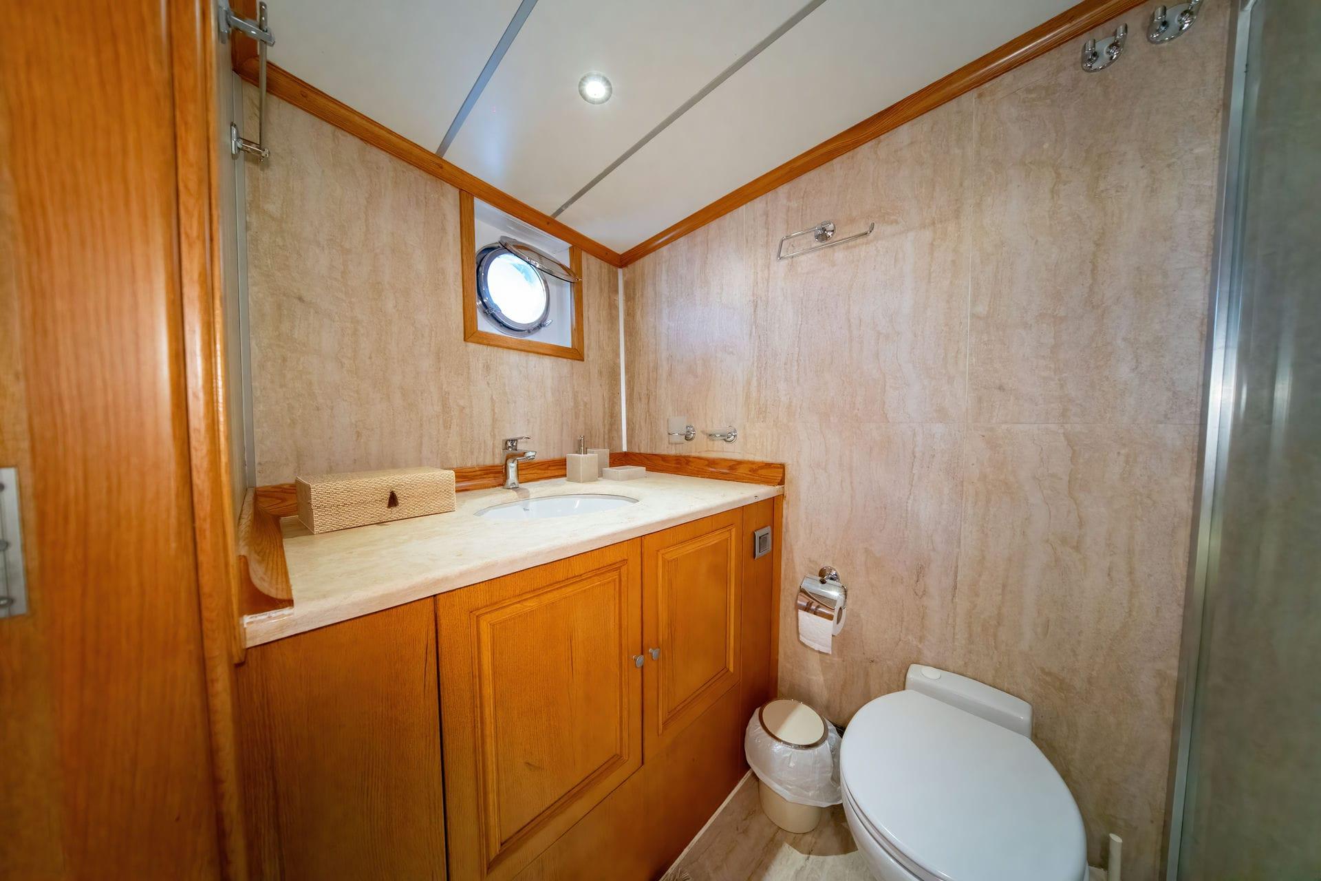 yacht guest bathroom with marble walls, wooden vanity, porthole window and toilet