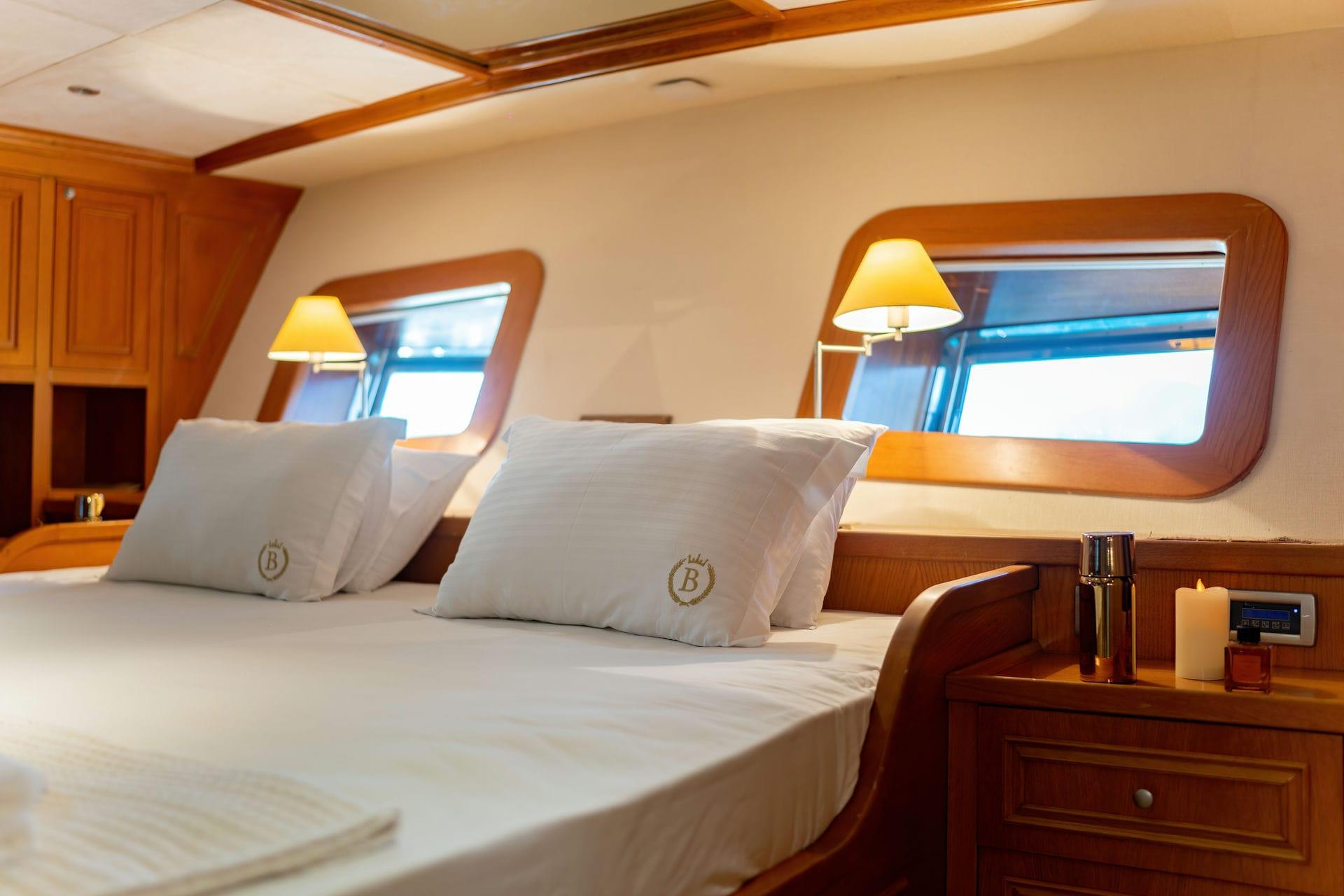 yacht guest cabin featuring double bed with white linens and two rounded portholes with reading lights