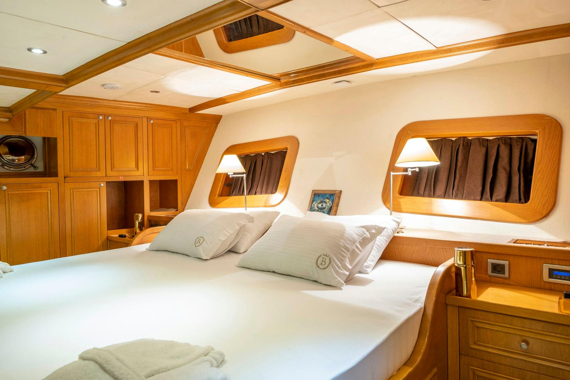 yacht cabin interior with double bed, wooden cabinetry, and two oval portholes with curtains